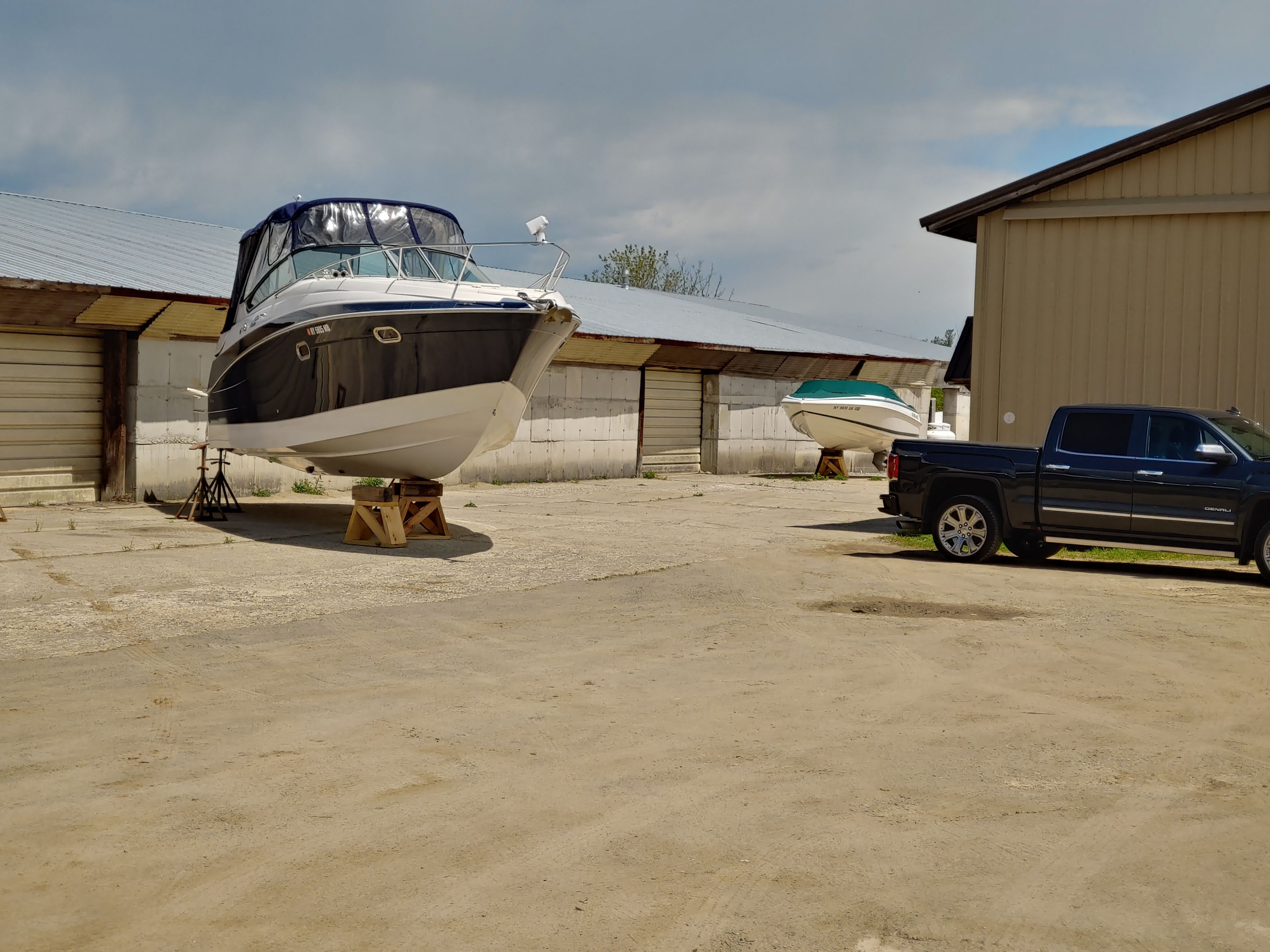 A boat is on a dry dock next to a building and a black pickup truck.