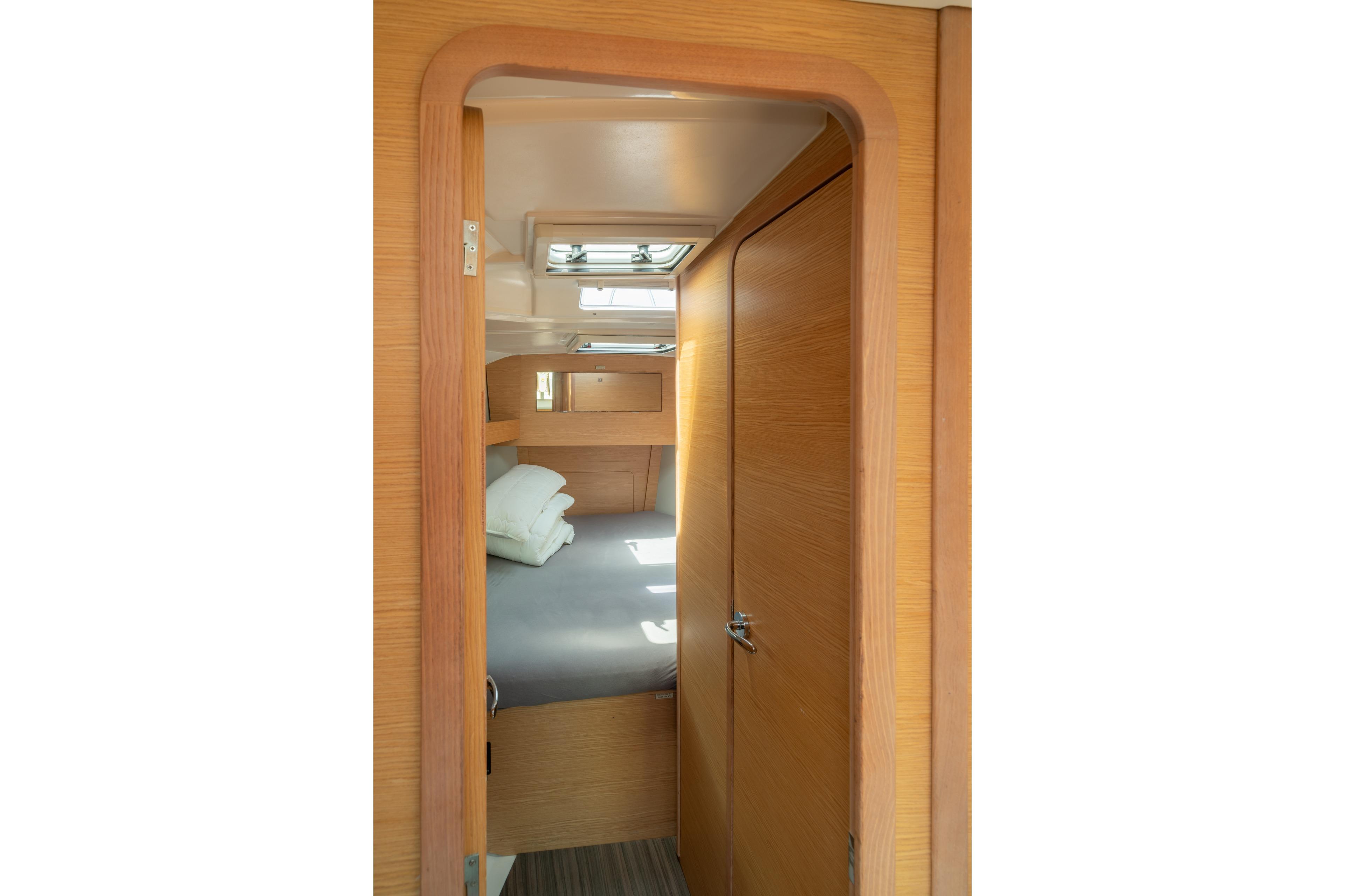 Interior cabin view of 2021 Dufour 390 yacht, featuring wooden door and cozy bed.