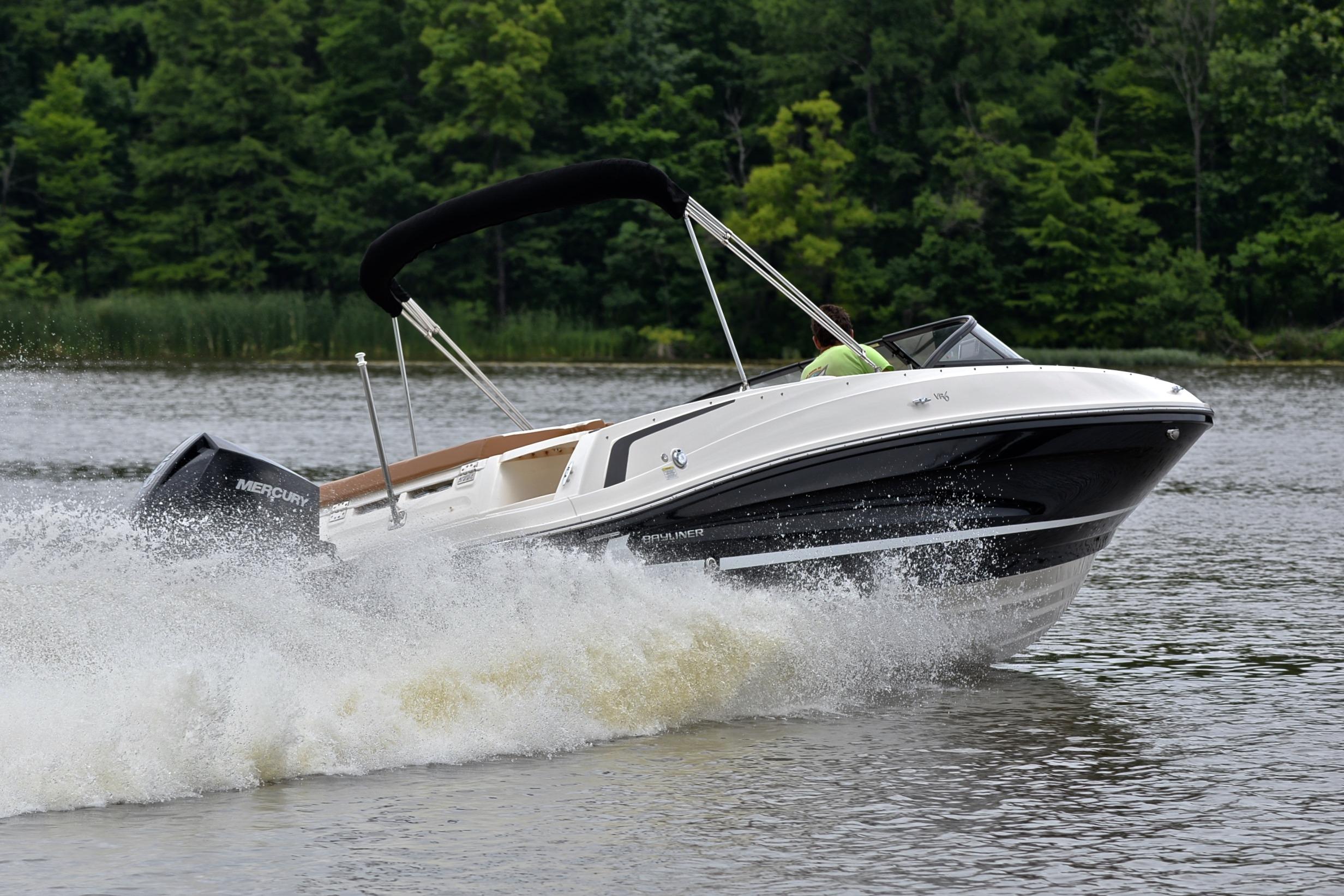 2019 Bayliner VR6 Bowrider OB speeding on a lake with lush green background.