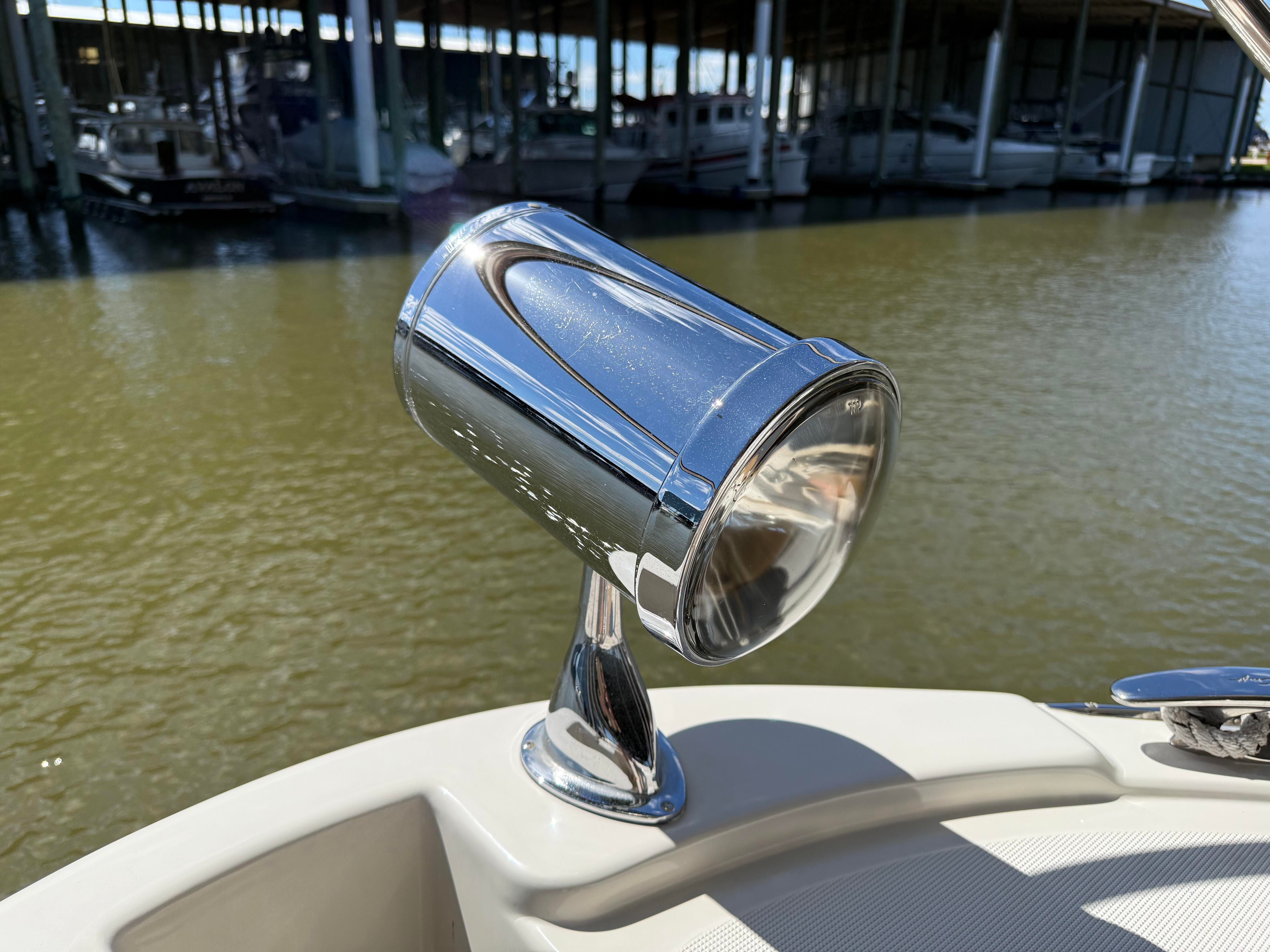 Close-up of a chrome spotlight on a boat, with water and a dock in the background.