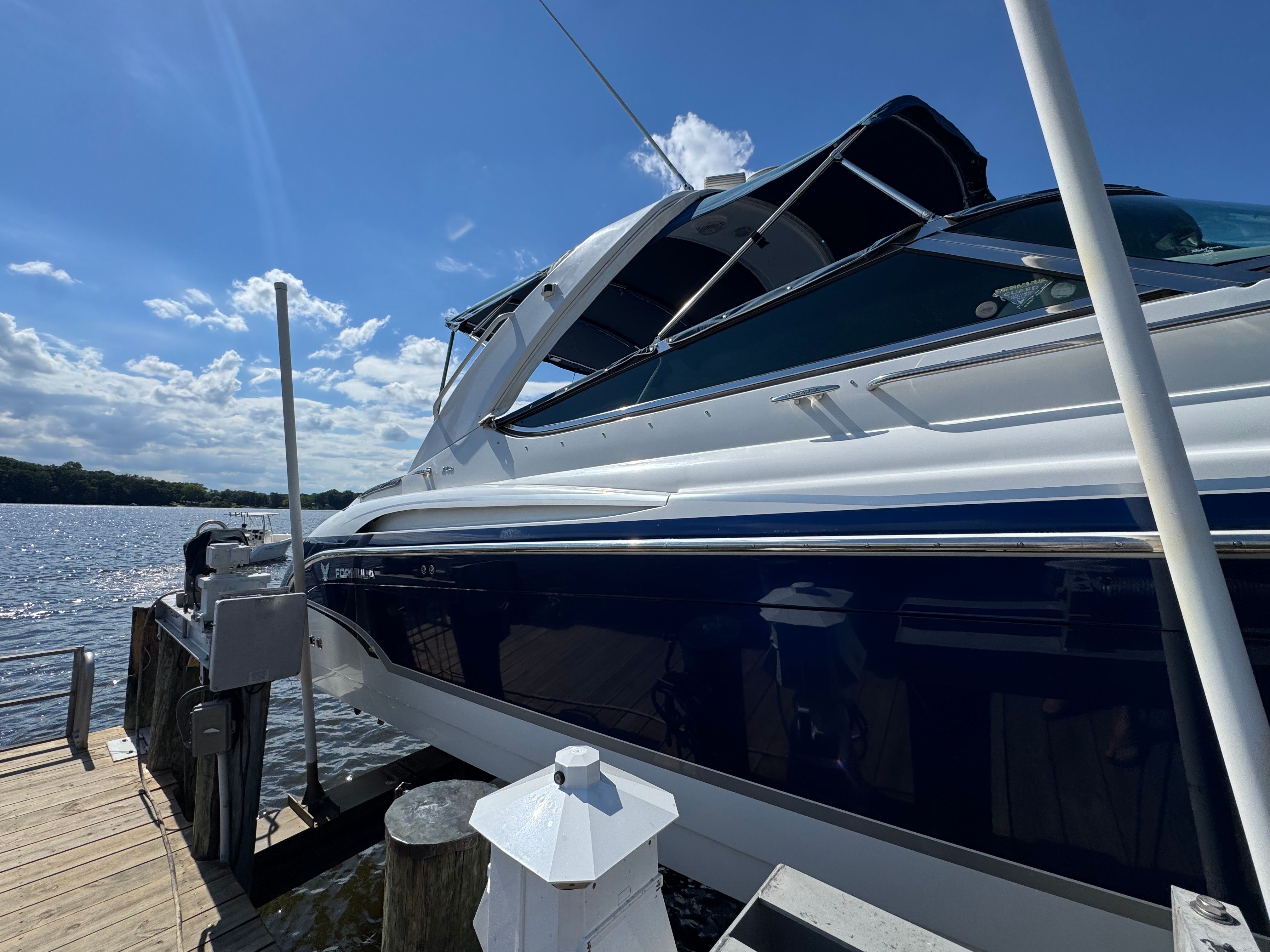 A white and blue boat docked at a wooden pier under a blue sky.
