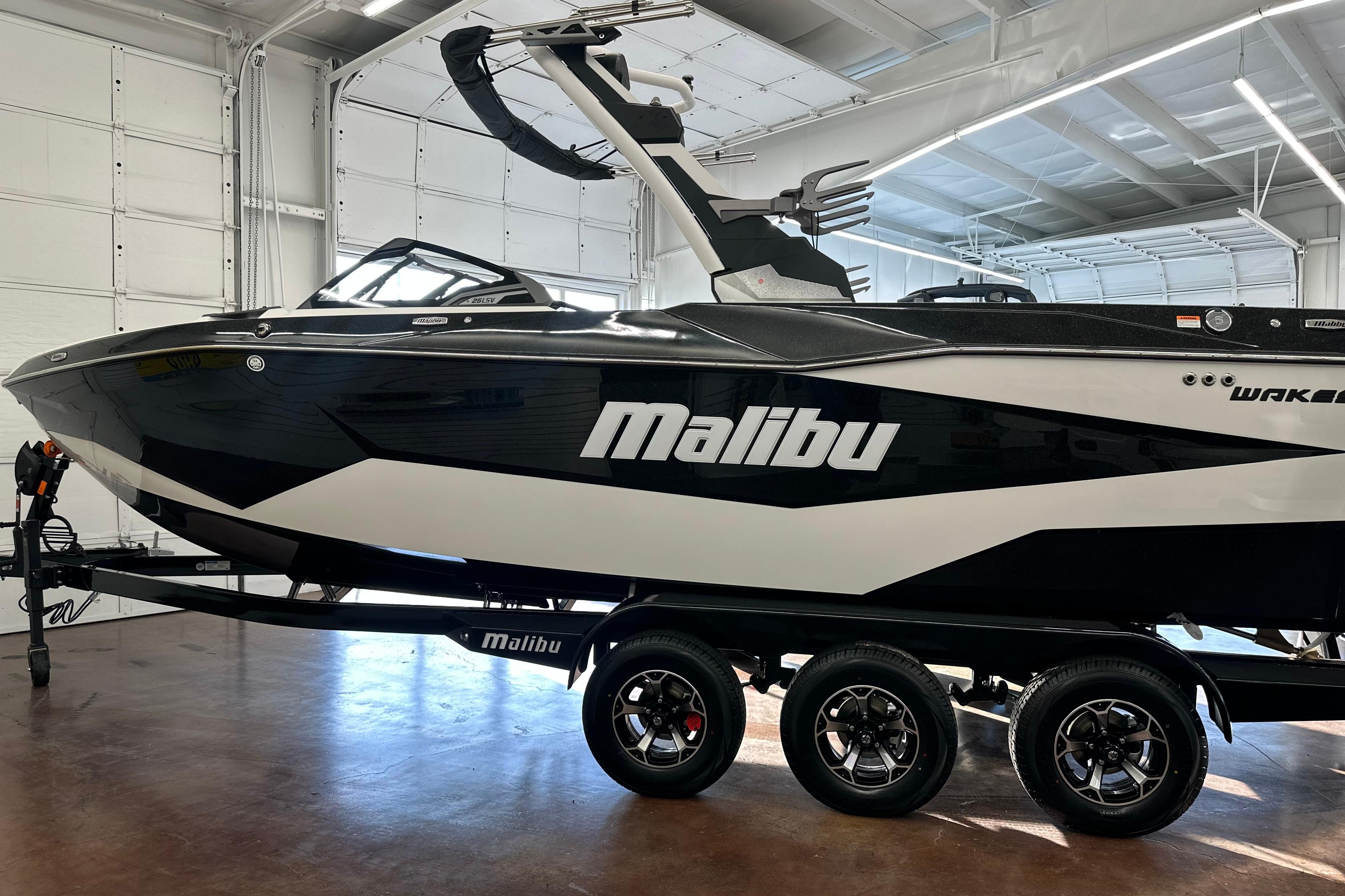 2026 Malibu Wakesetter 25 LSV boat in showroom, black and white design, on trailer.
