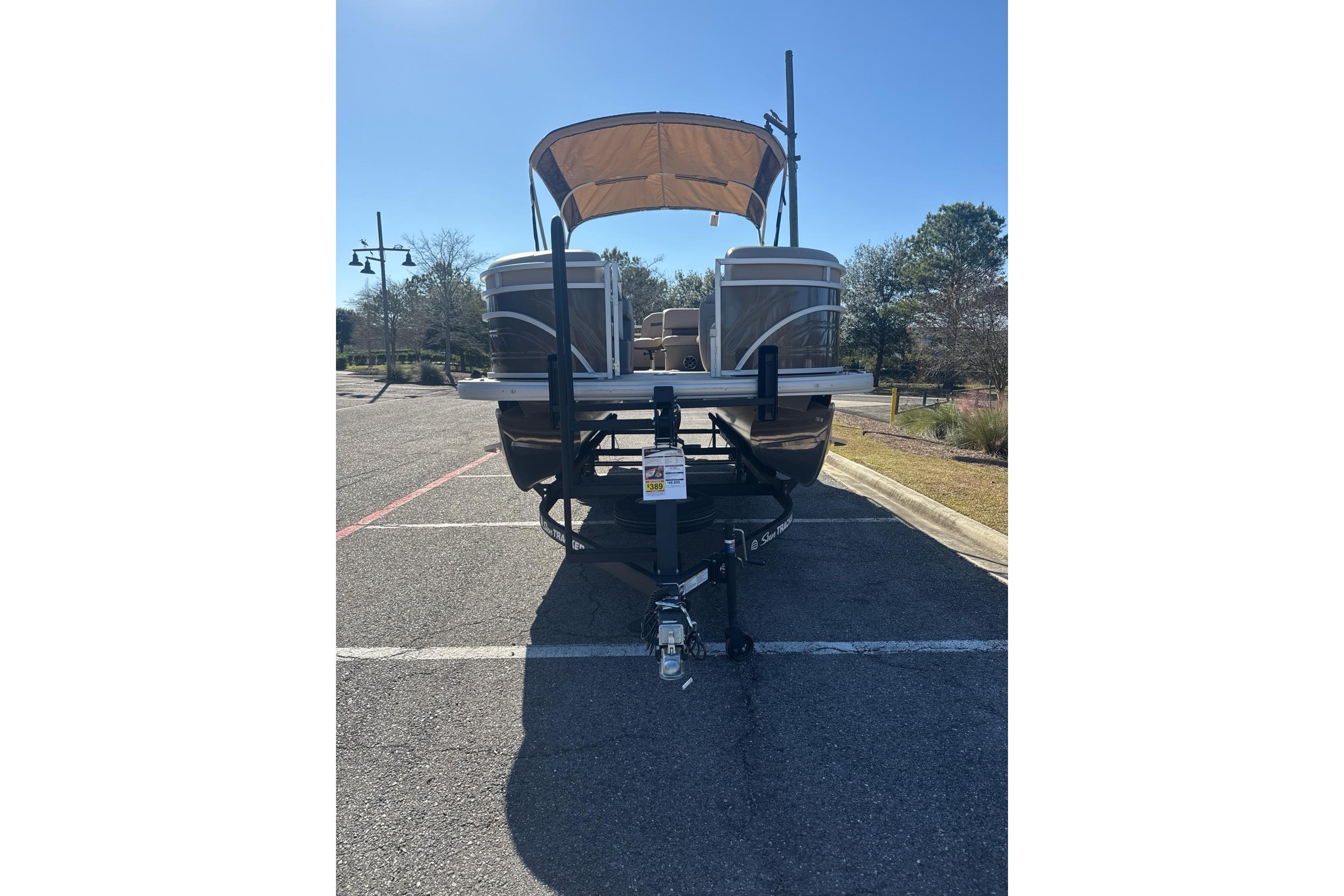 2025 Sun Tracker SportFish 22 DLX pontoon boat on trailer in parking lot.