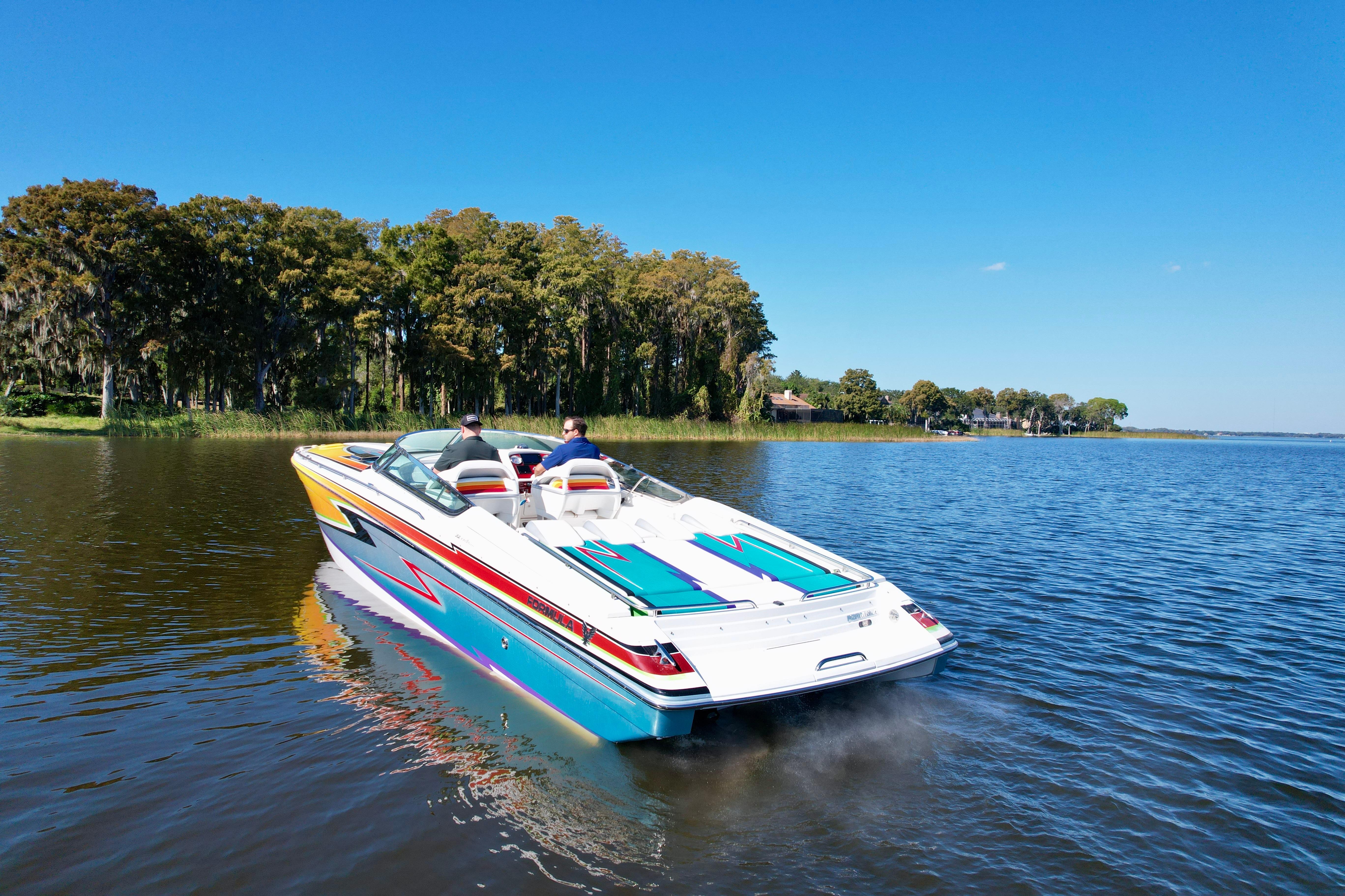 2006 Formula 382 FASTech boat cruising on a serene lake with lush green shoreline.