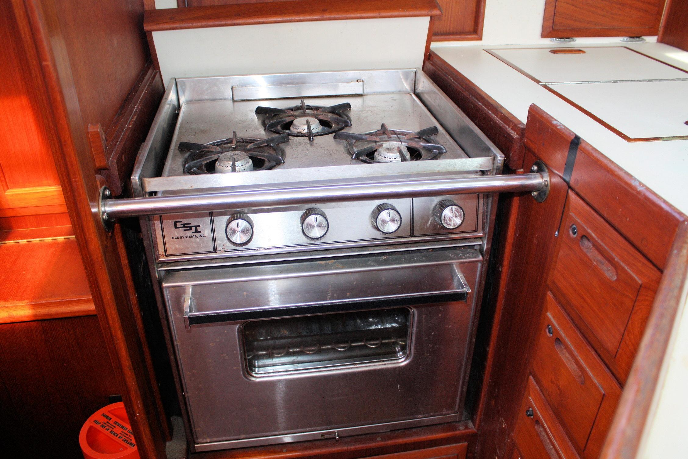 Stainless steel stove in 1987 Ericson 38-200 yacht kitchen, featuring three burners and wooden cabinetry.
