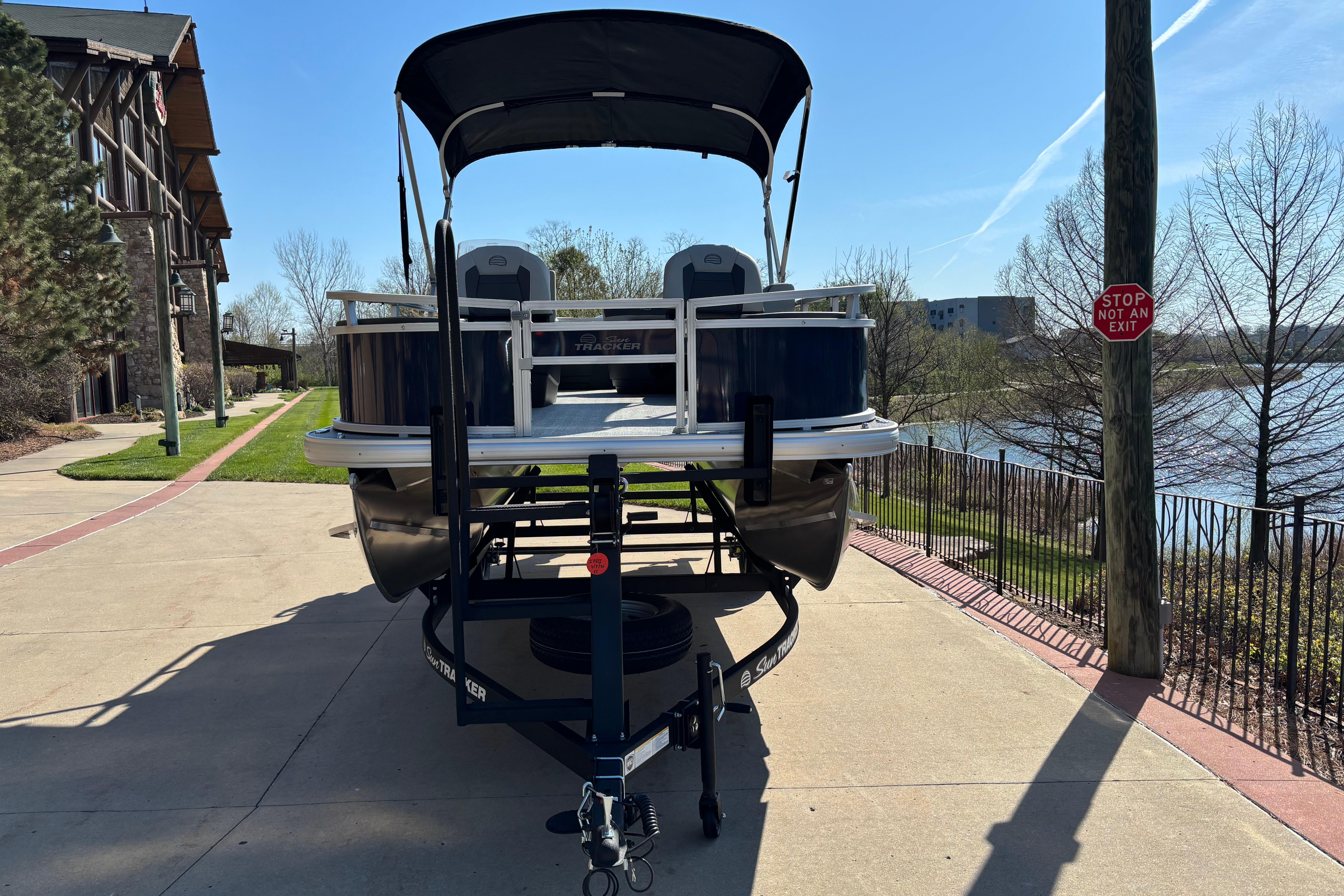 2026 Sun Tracker Bass Buggy 18 DLX pontoon boat on trailer, parked near a scenic lake.