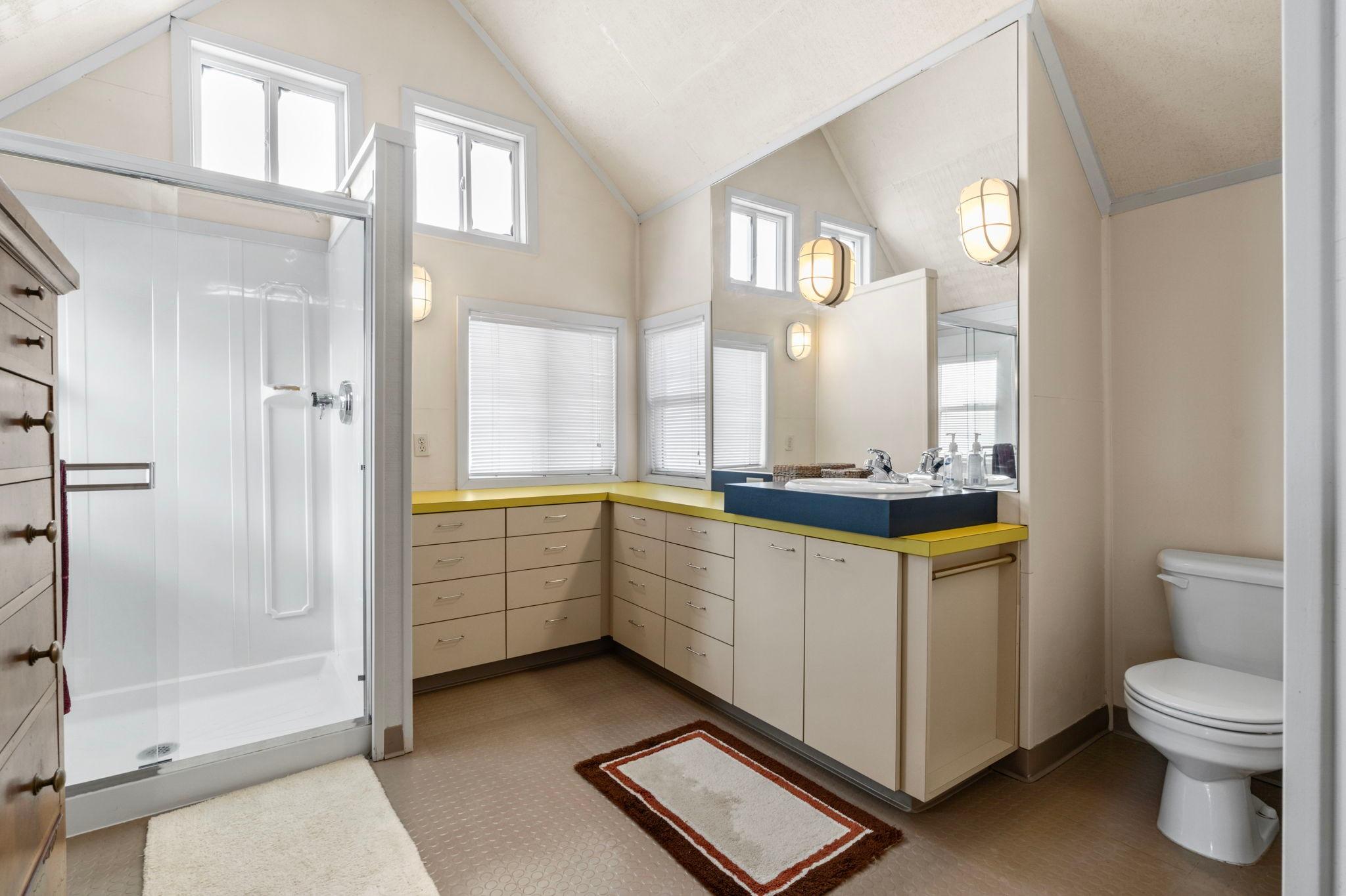 Spacious 1976 custom boathouse bathroom with shower, vanity, and toilet, featuring ample natural light.