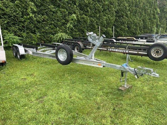 A boat trailer sits on a grassy area, surrounded by trees and other trailers.