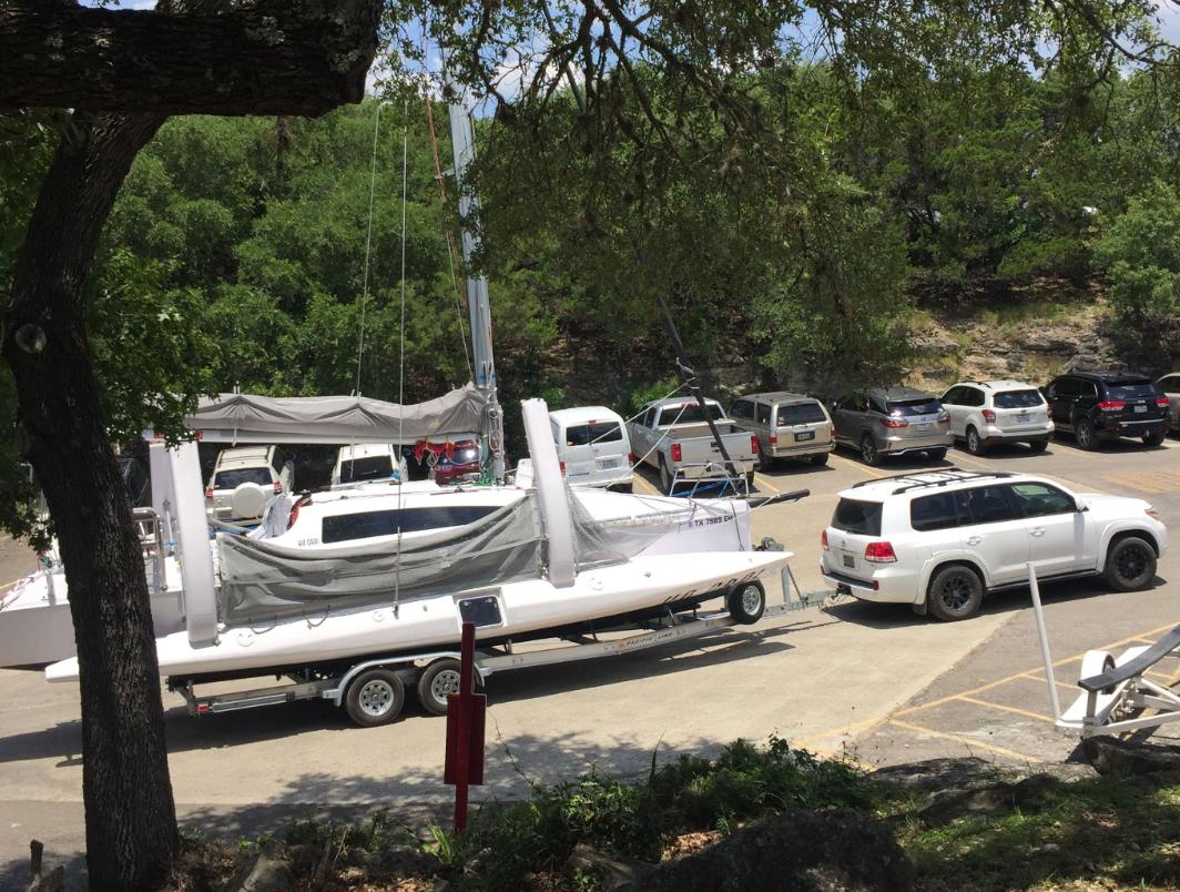 Corsair 970 sailboat on trailer in parking lot, surrounded by trees and vehicles, 2025 model.
