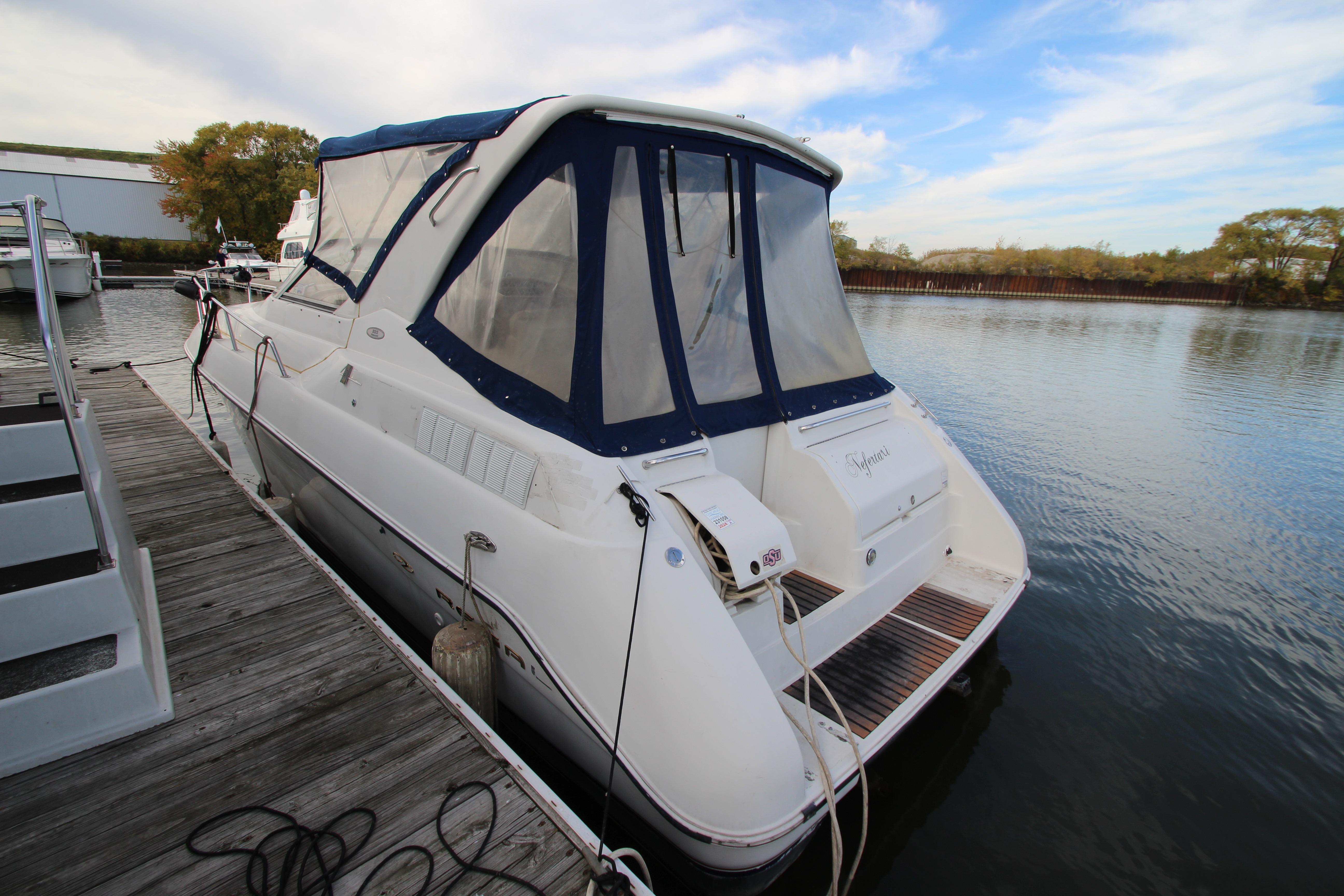 1999 Regal Commodore 322 boat docked at a marina, featuring a blue canopy.