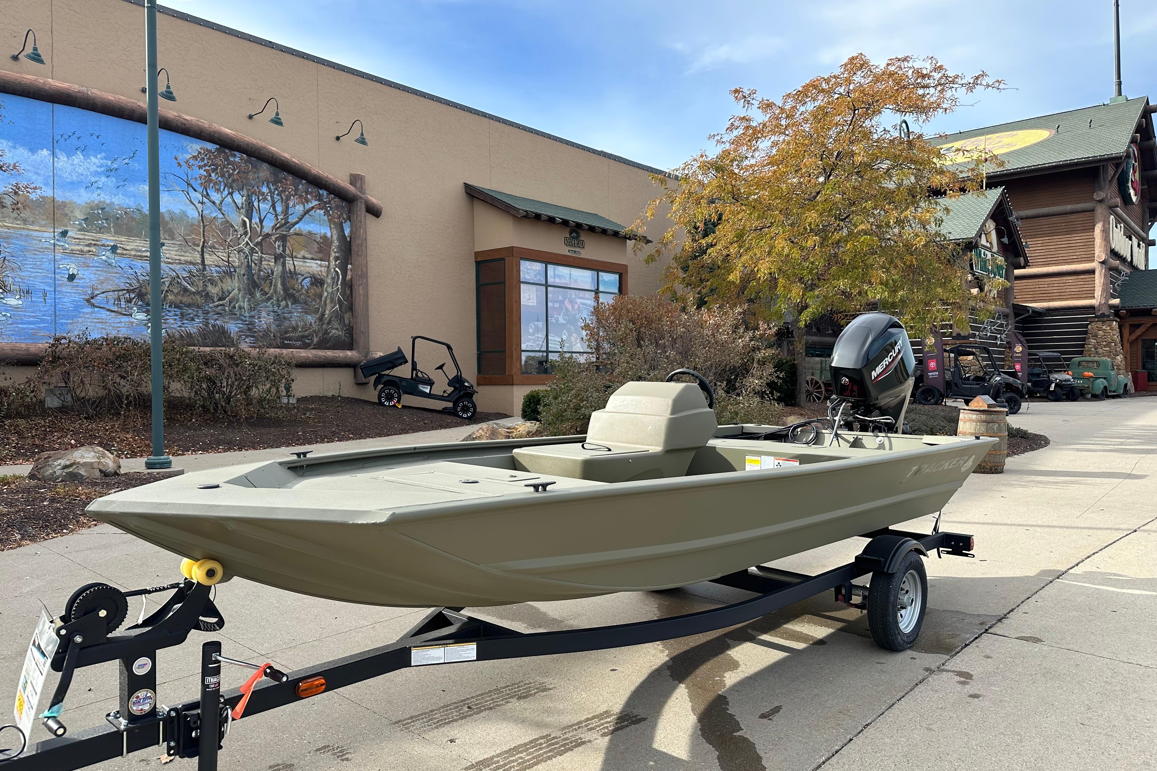 2026 Tracker Grizzly 1648 SC boat on trailer outside a building with mural.