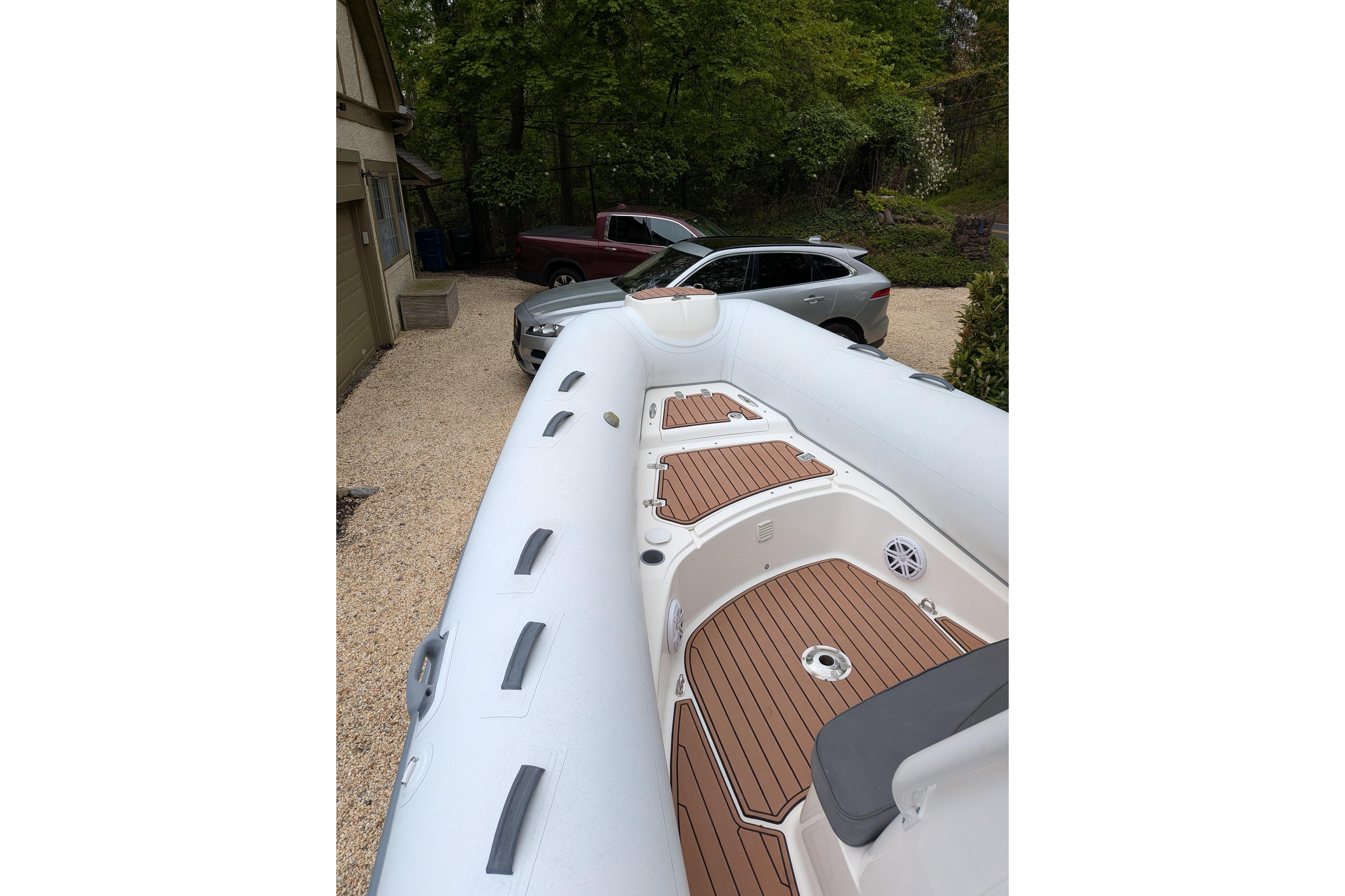 2016 Brig E780 inflatable boat with wooden deck, parked near cars in a driveway.