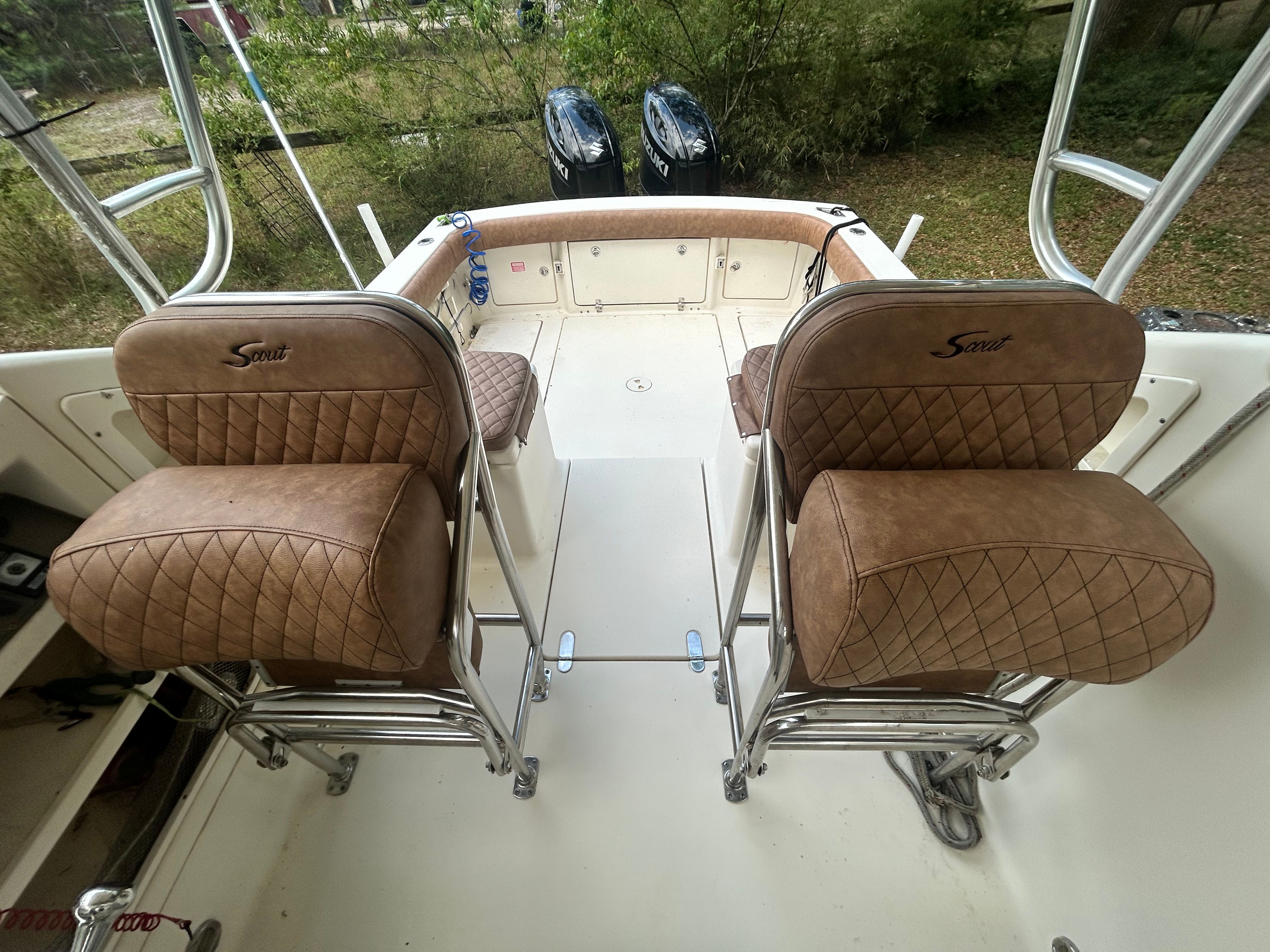 Two cushioned seats with quilted leather on a boat, surrounded by green vegetation.