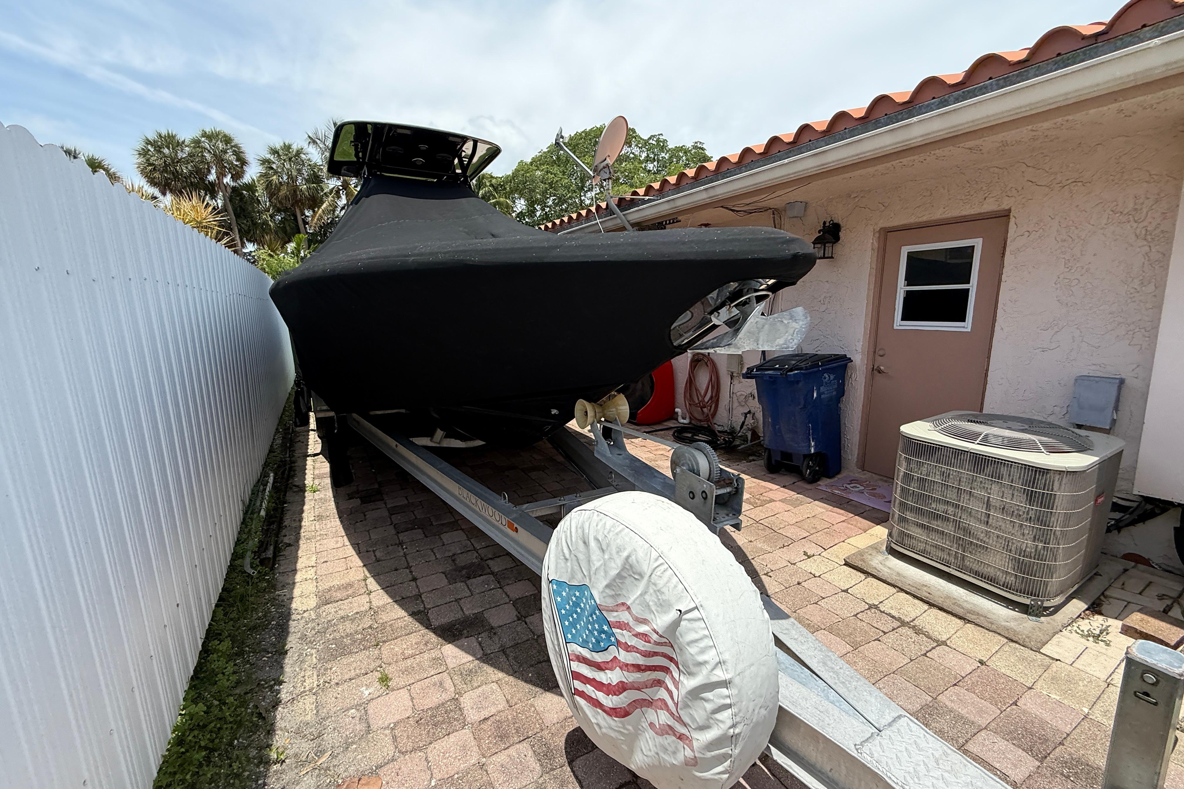 Covered Blackwood 27 boat on trailer beside house, American flag tire cover, 2015 model.