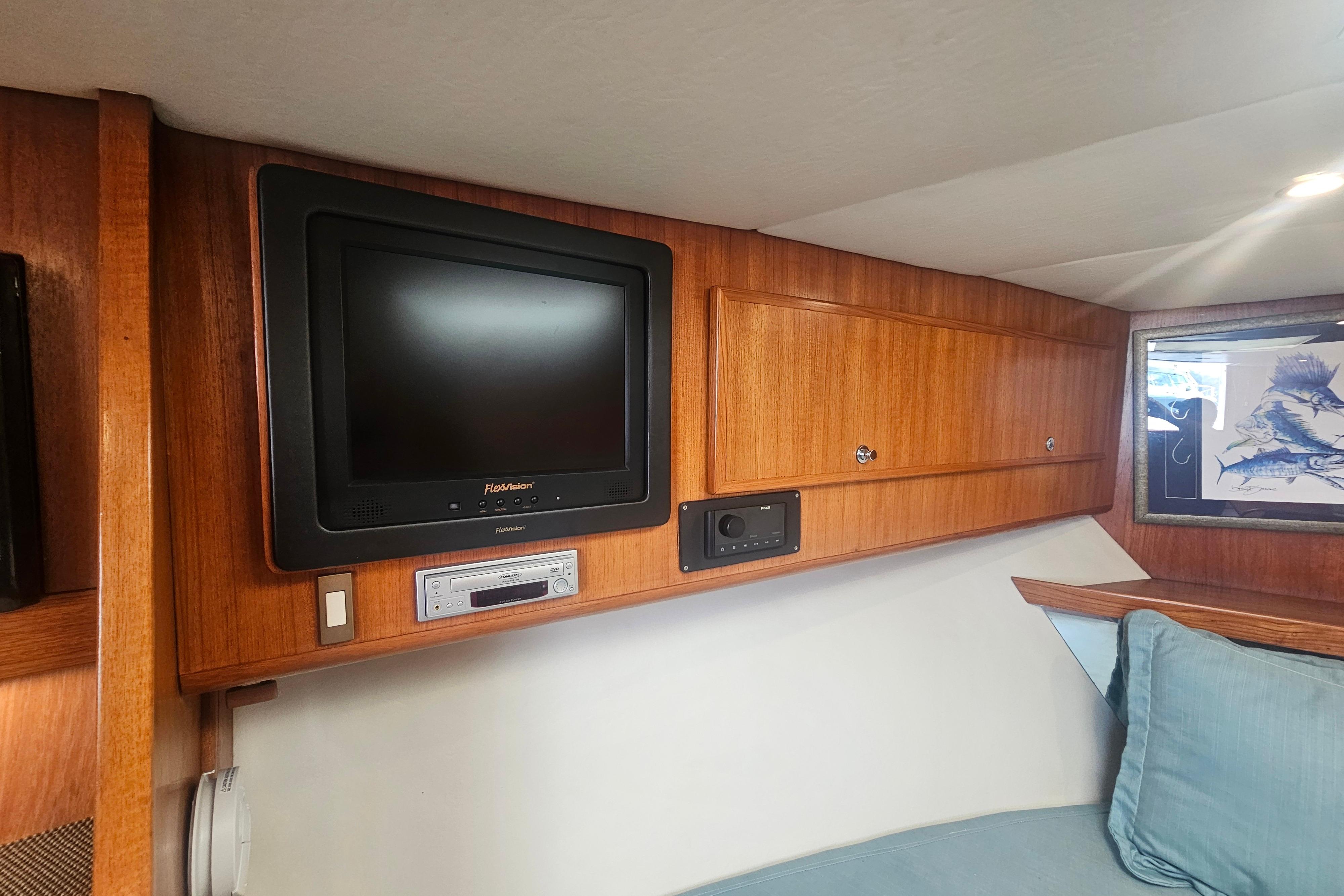 Interior of 2003 Topaz 32 Express boat with TV, wooden cabinets, and blue cushions.