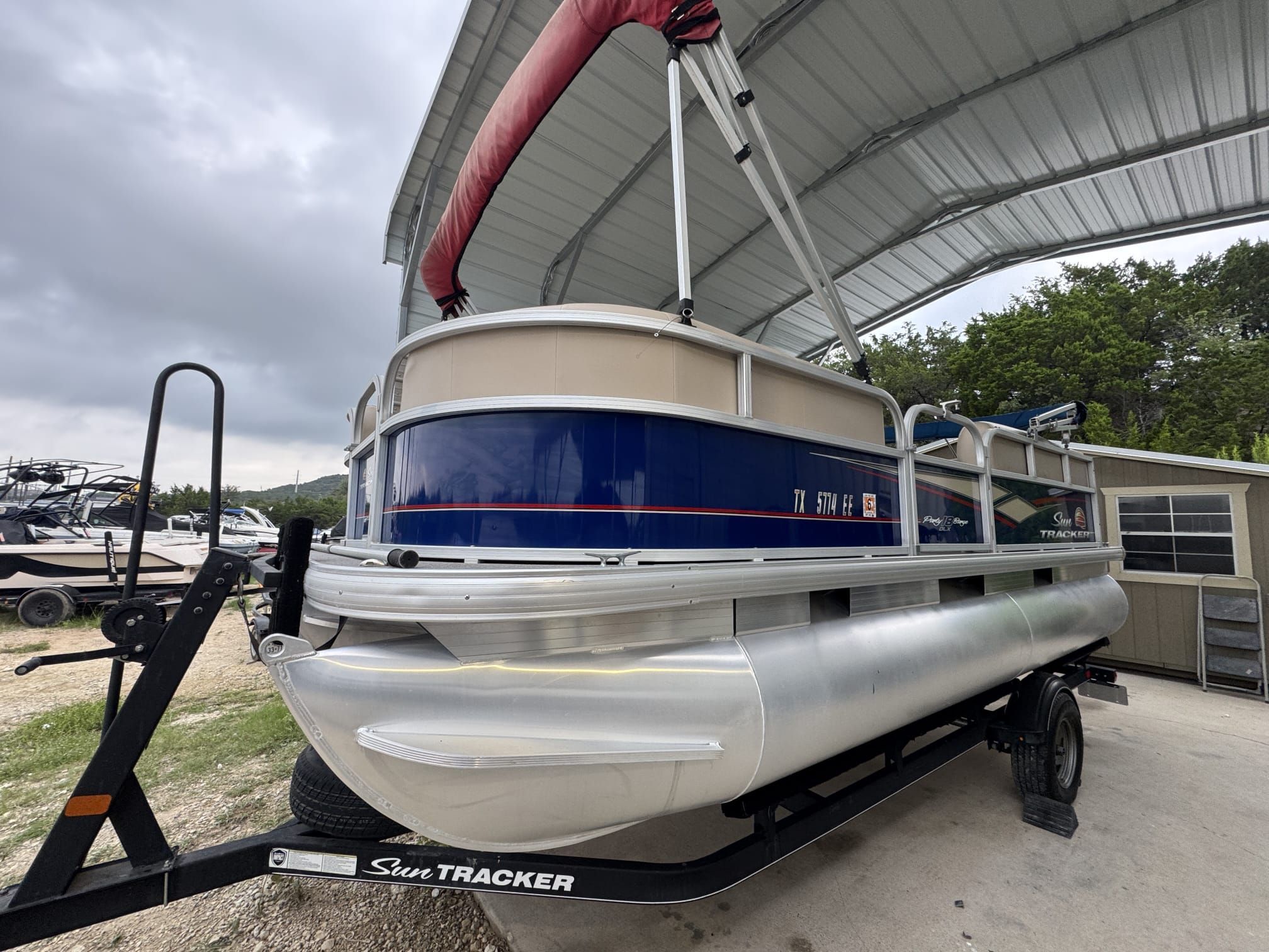 A 2018 Sun Tracker Party Barge 18 DLX on a trailer under a covered area.