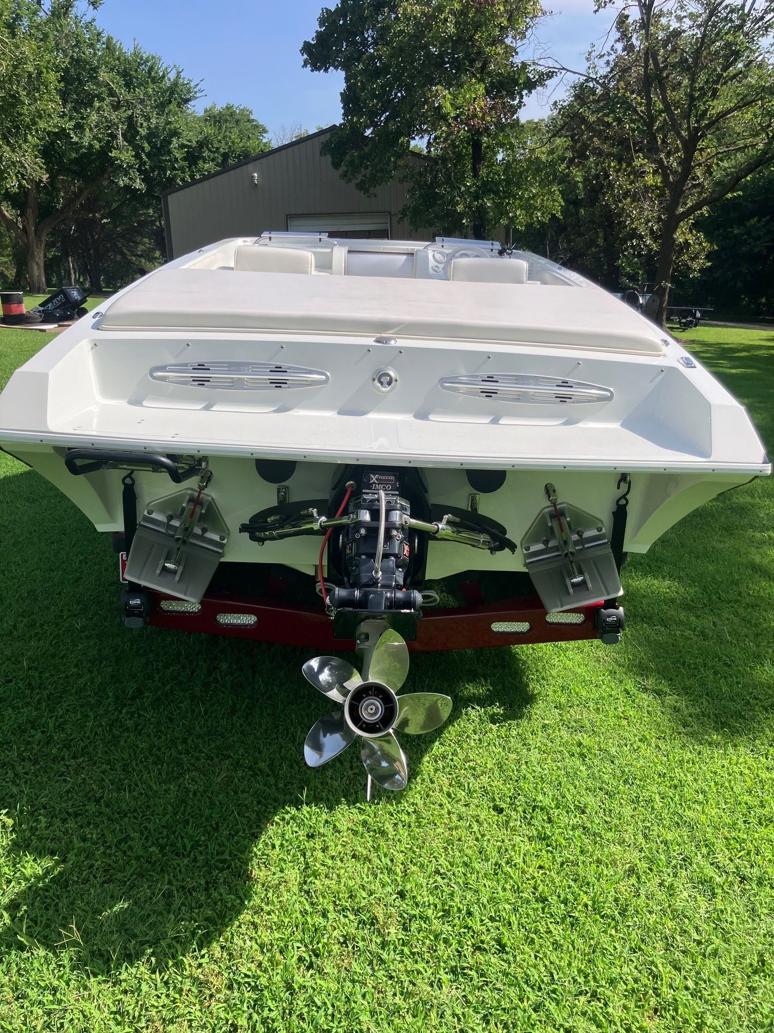 Rear view of a white boat on grass with visible propeller.