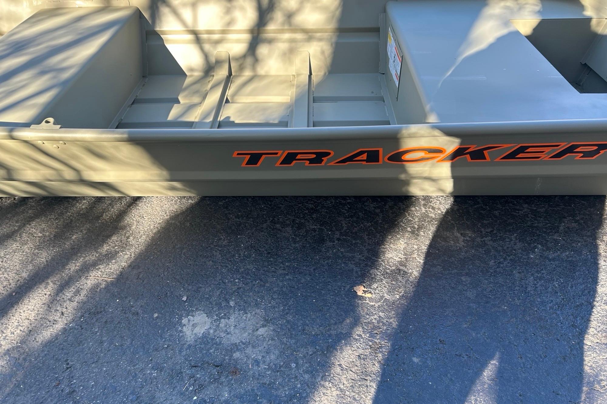 2026 Tracker Grizzly 14 Jon boat, olive green, parked on pavement with shadows.