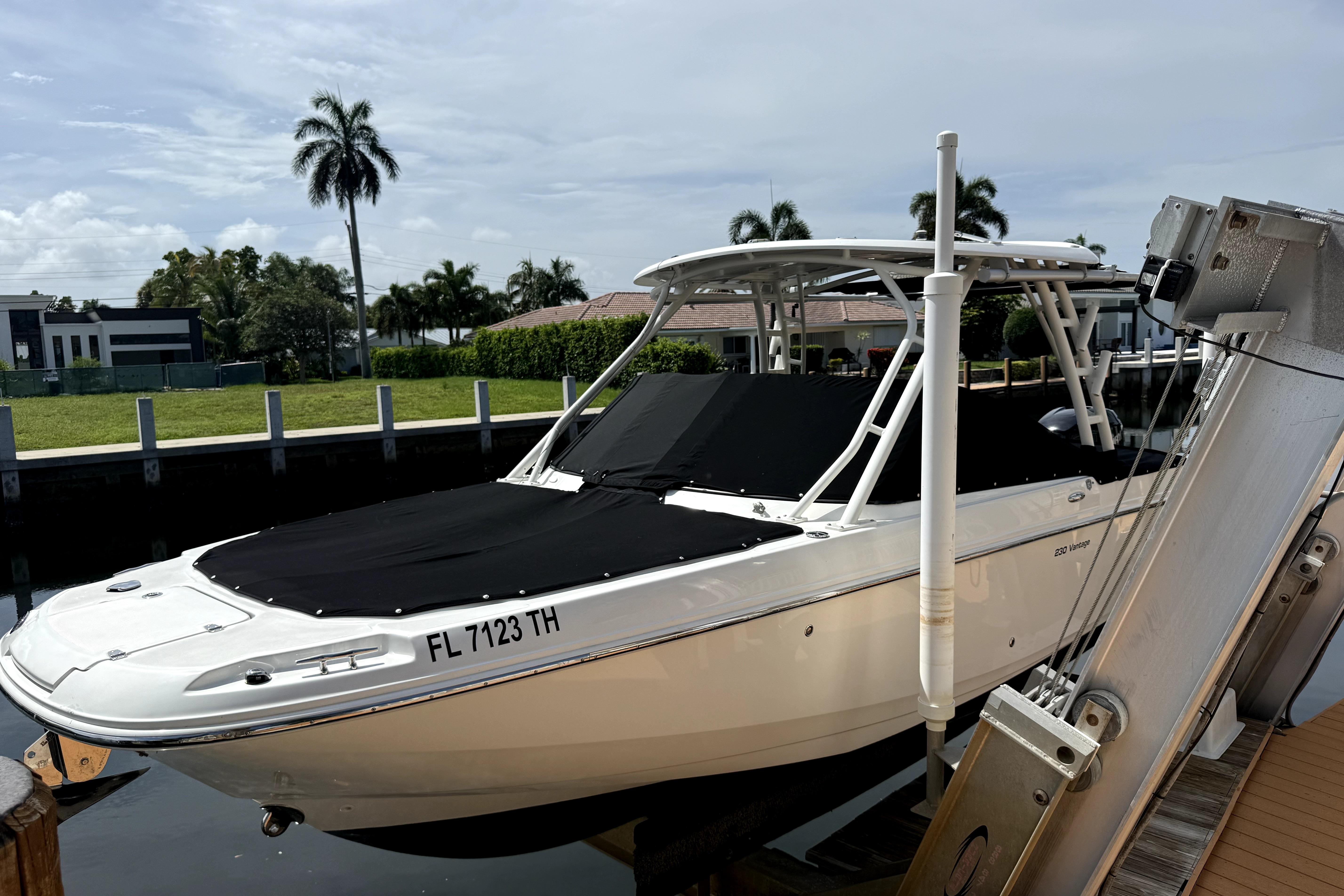 2018 Boston Whaler 230 Vantage boat docked, covered, with palm trees in the background.