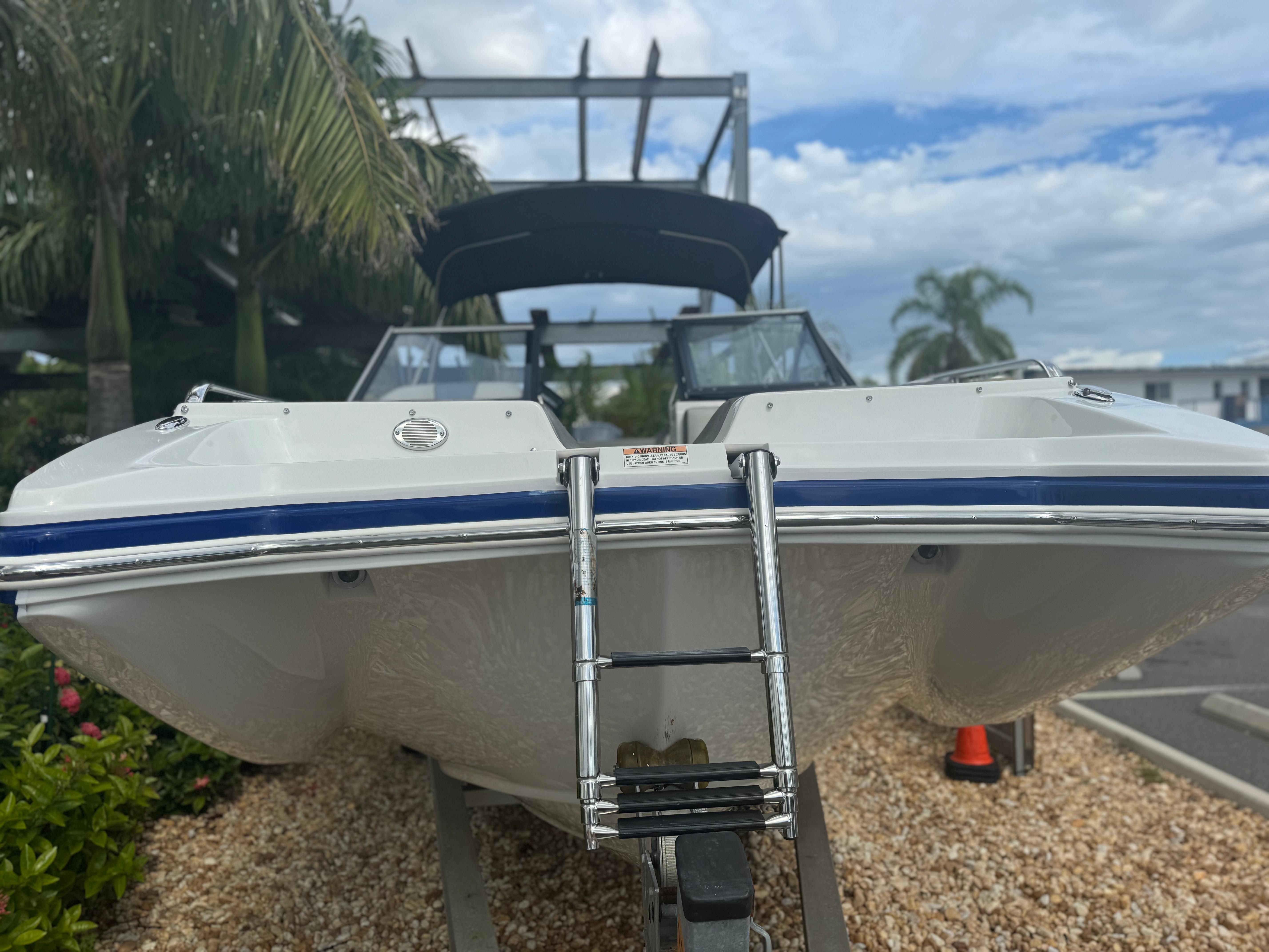2017 Starcraft 230 OB SCX EXT boat on trailer, surrounded by palm trees and gravel.
