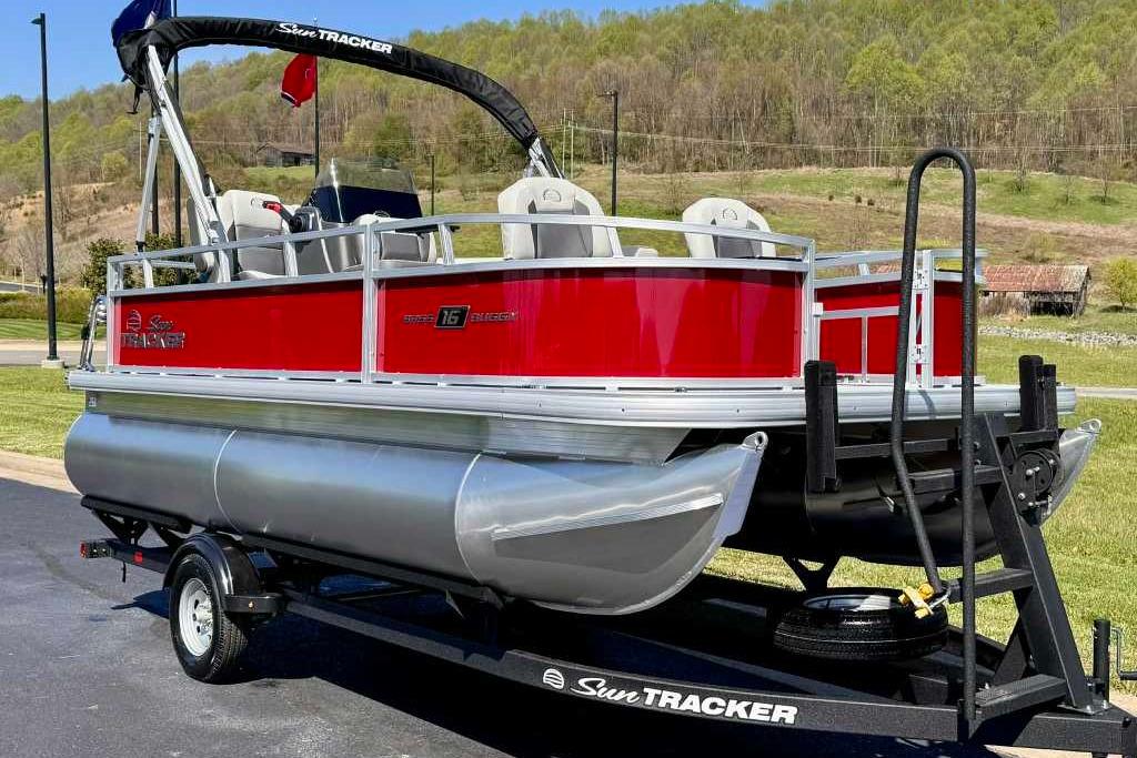 2026 Sun Tracker Bass Buggy 16 XL Select pontoon boat on trailer, red and silver design.