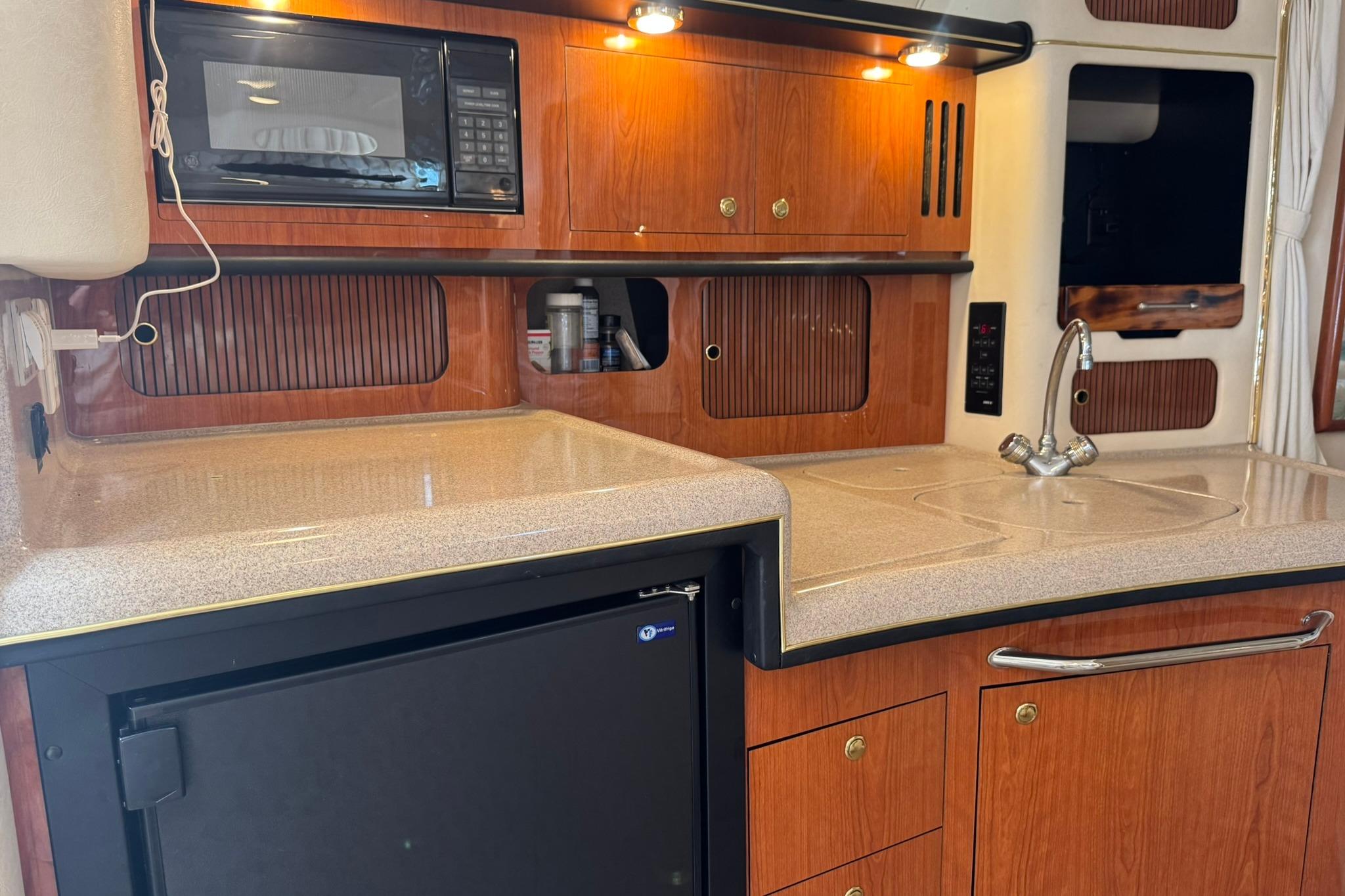 2001 Sea Ray 340 Sundancer galley with wood cabinetry, microwave, and compact refrigerator.