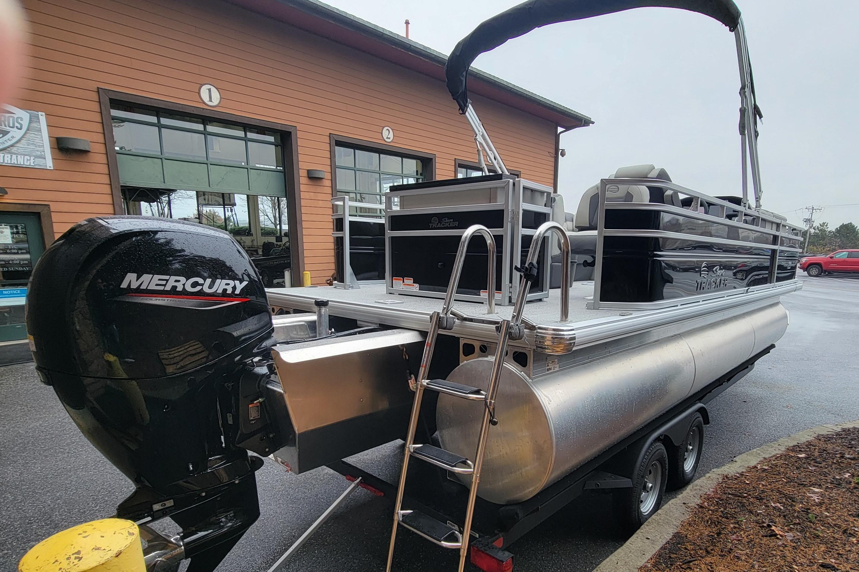 2026 Sun Tracker Fishin' Barge 22 XP3 pontoon boat with Mercury engine, parked outside.