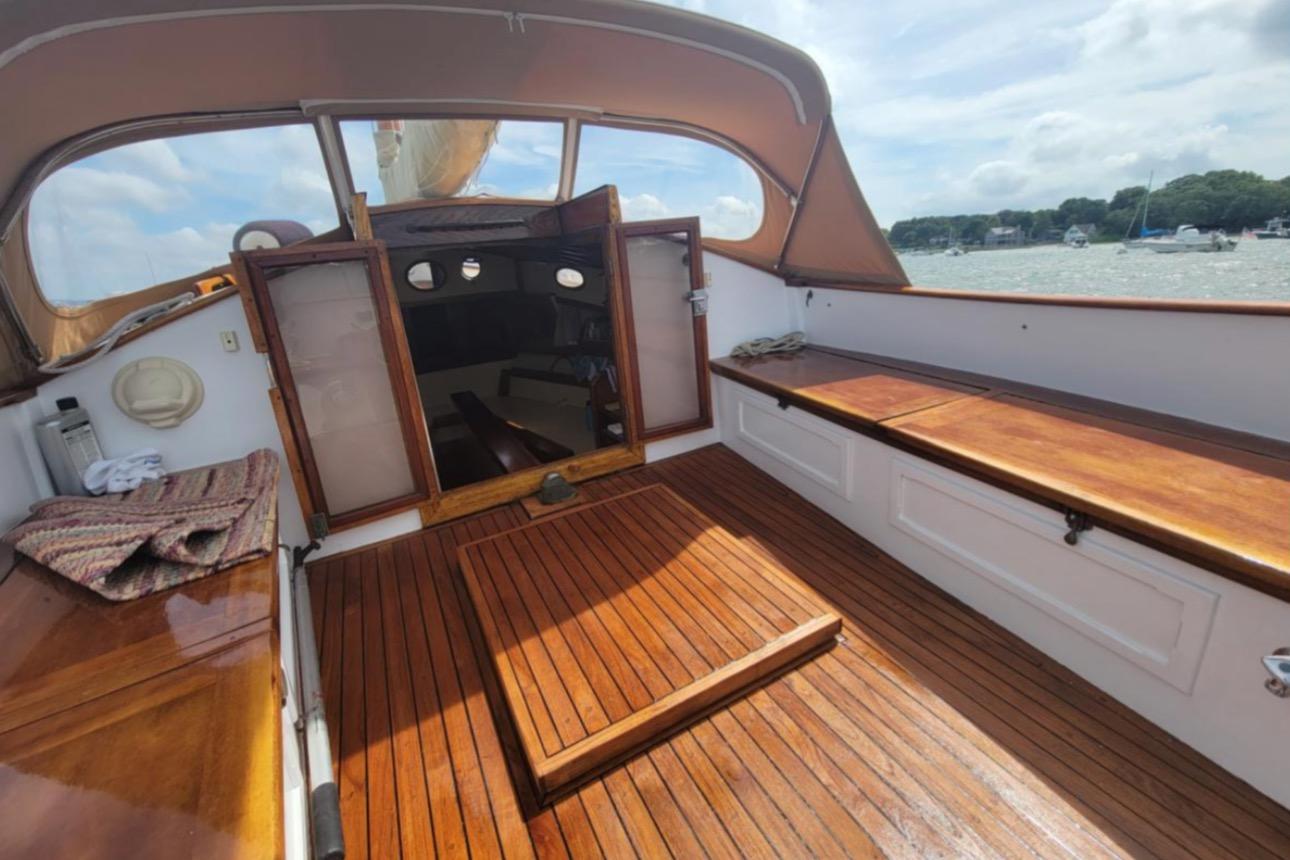 1978 Cape Cod Catboat interior with wooden deck, open cabin, and scenic water view.