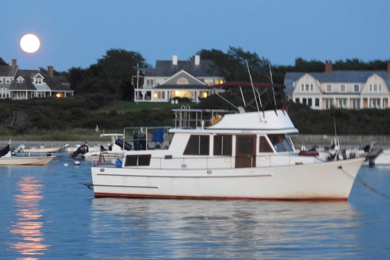 1987 Marine Trader 36 yacht anchored near coastal homes under a full moon.