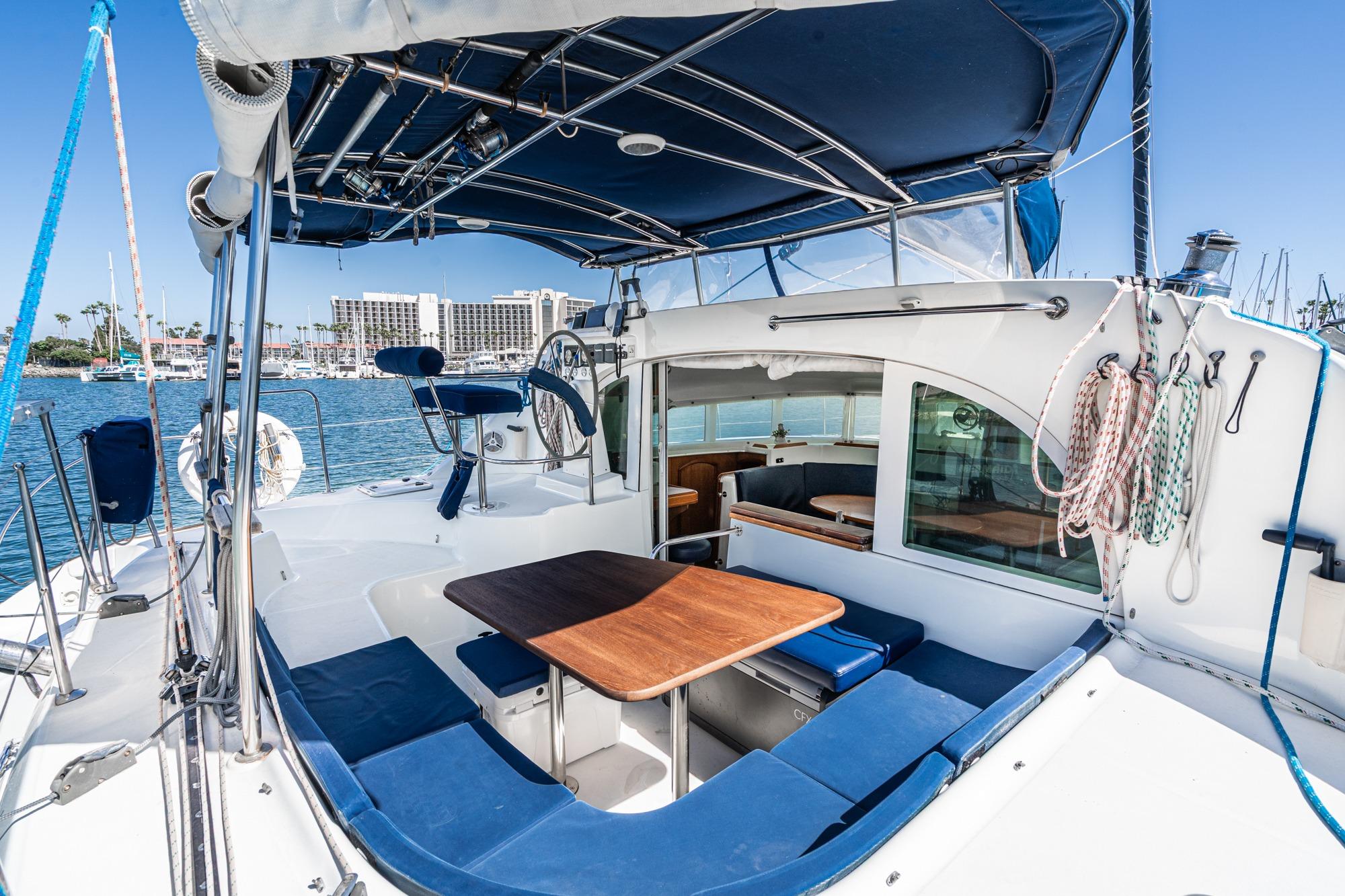 Lagoon 380 catamaran cockpit with blue seating, wooden table, and marina view, 2004 model.