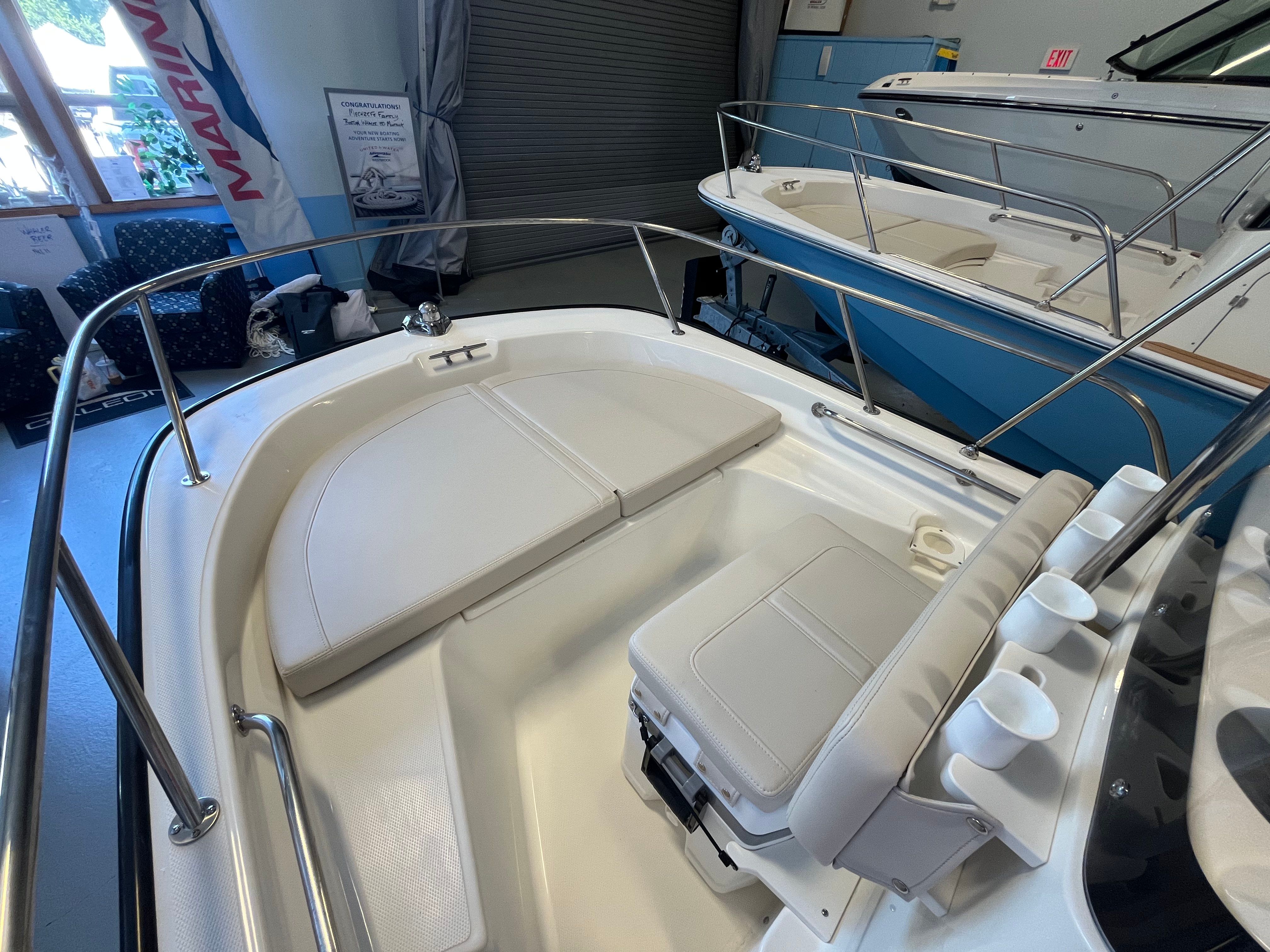 The image shows the cockpit of a Boston Whaler 150 Montauk with beige cushions and stainless steel railing.