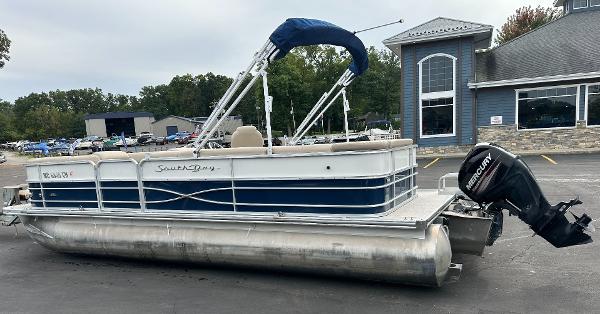 A 2018 South Bay S224CR pontoon boat is parked on a lot in front of a building.