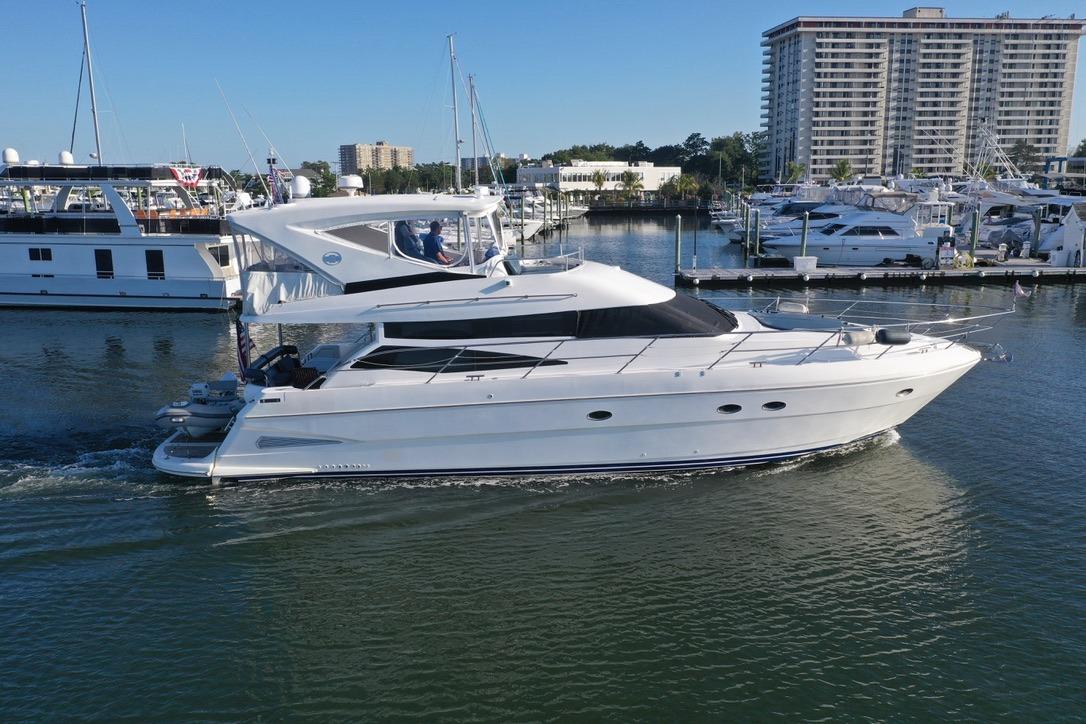 2005 Neptunus 56 Flybridge yacht cruising in a marina with modern buildings in the background.
