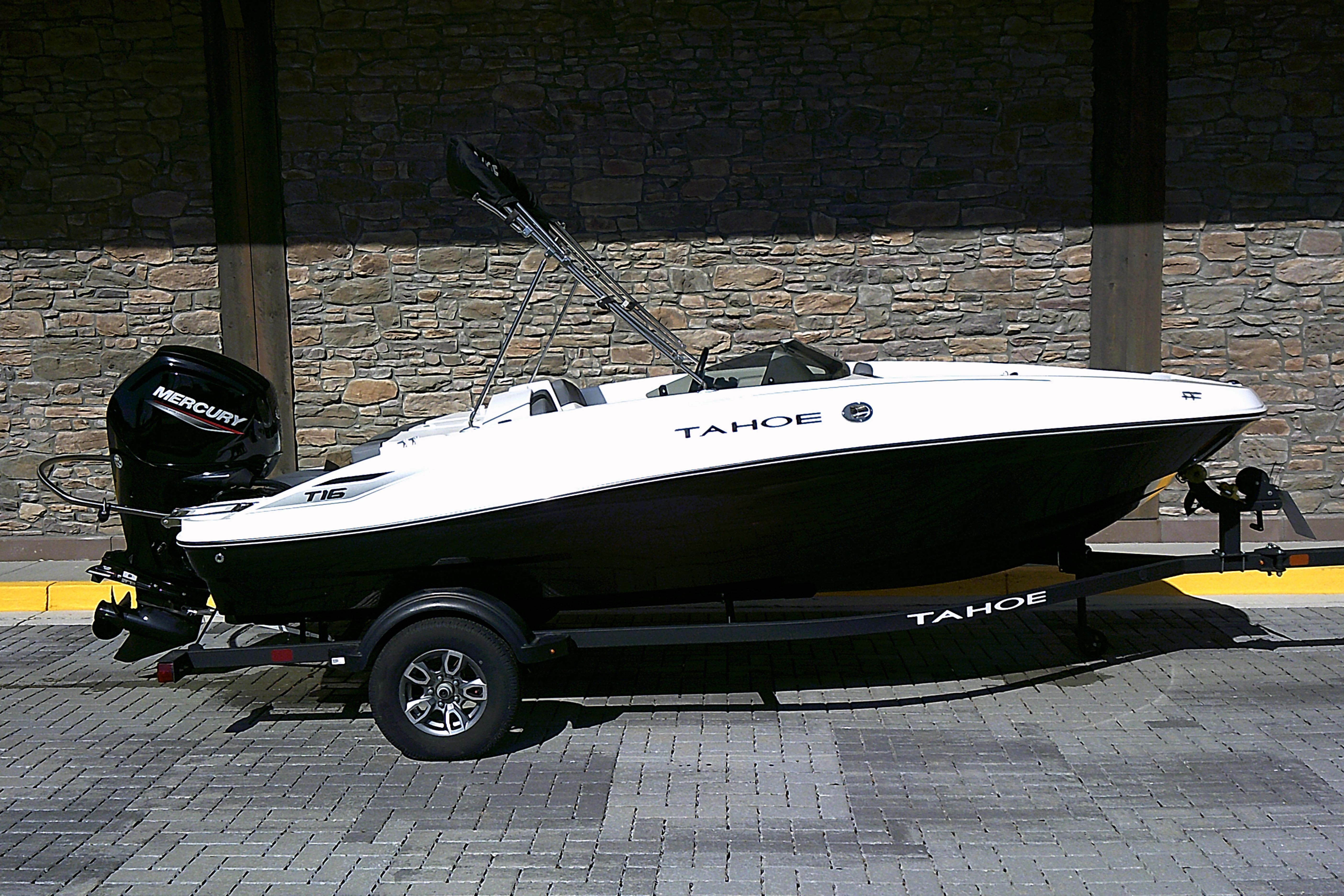 2025 Tahoe T16 boat with Mercury engine on trailer, parked on brick pavement.