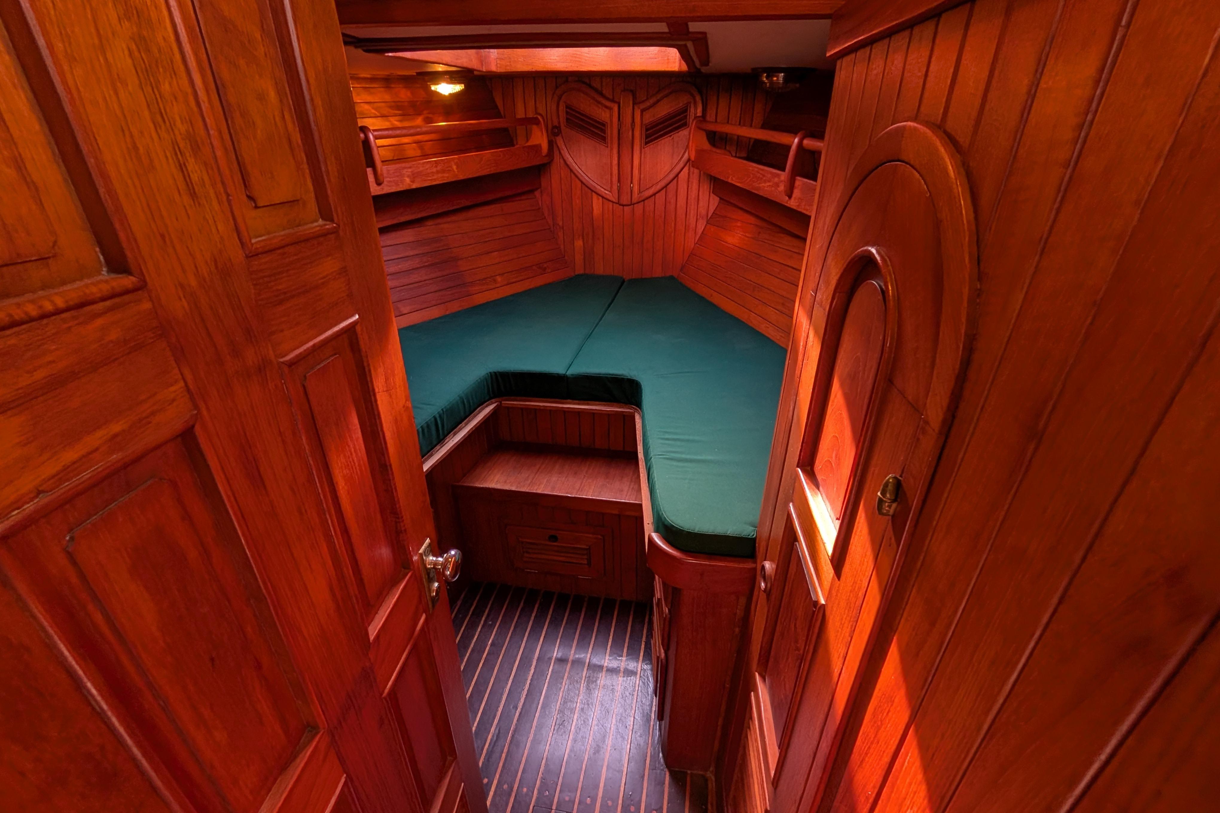 Cozy wooden cabin interior of 1983 Robert Perry 41 sailboat with green bedding.
