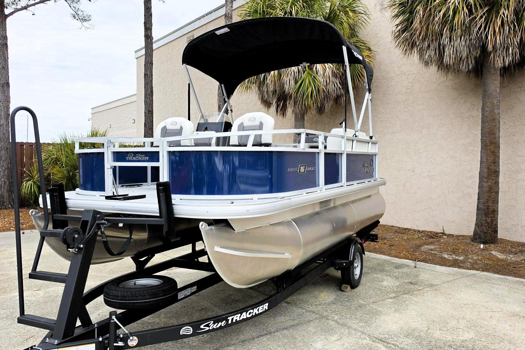 2026 Sun Tracker Bass Buggy 16 XL Select pontoon boat on trailer, parked outdoors.