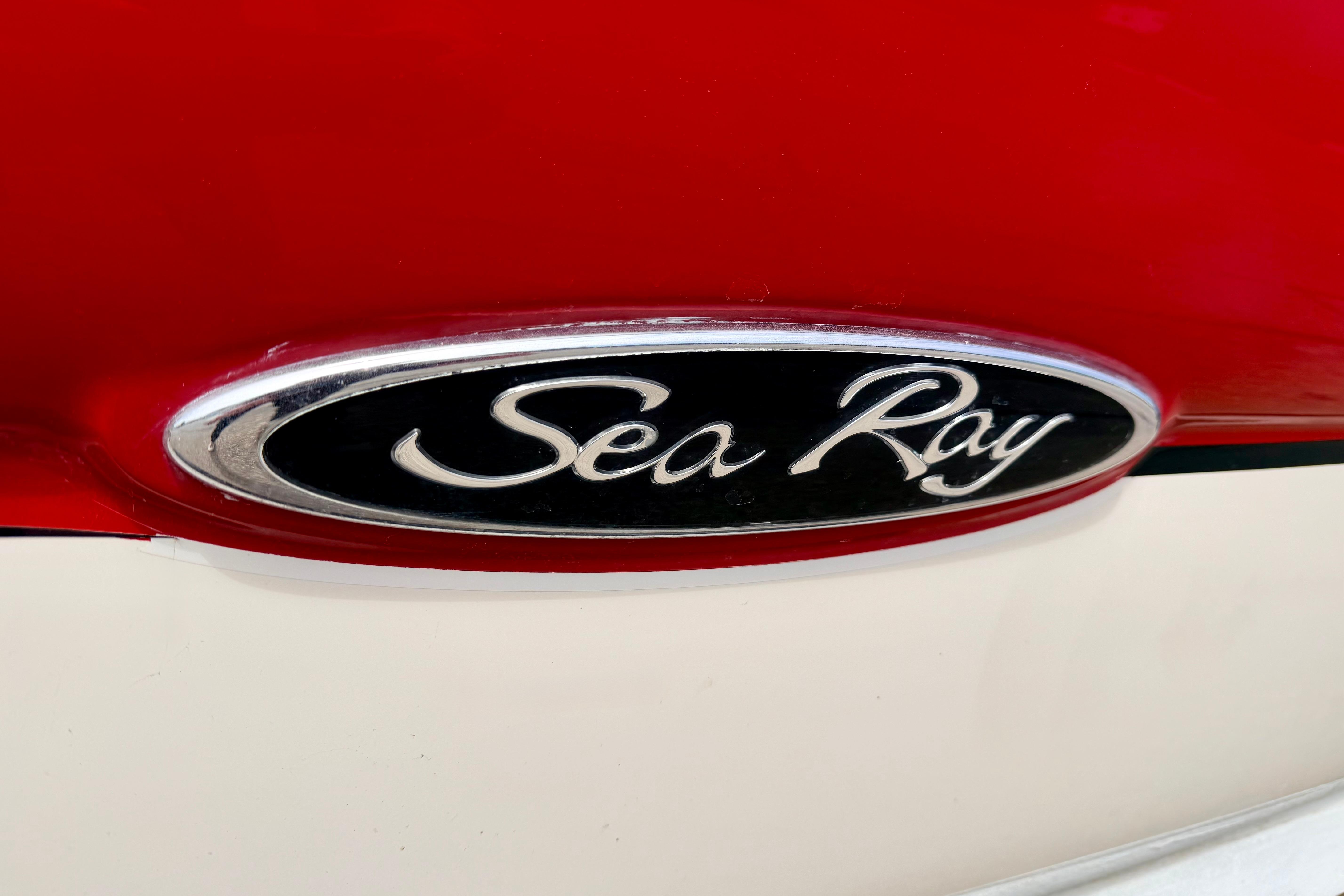 Close-up of 2003 Sea Ray 200 Sundeck logo on red and white surface.