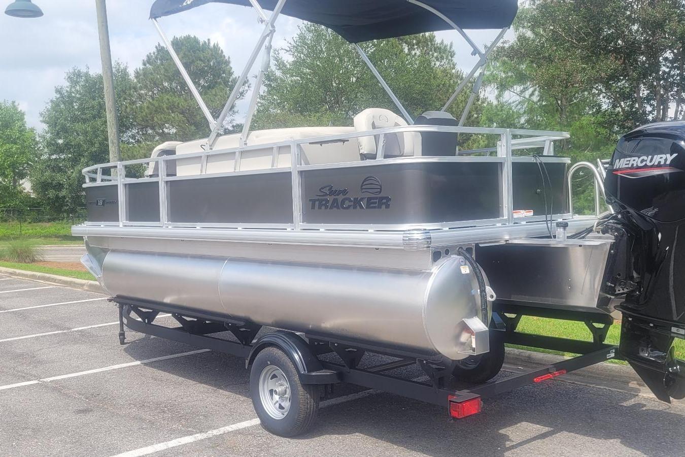 2026 Sun Tracker Bass Buggy 18 DLX pontoon boat on trailer in parking lot.