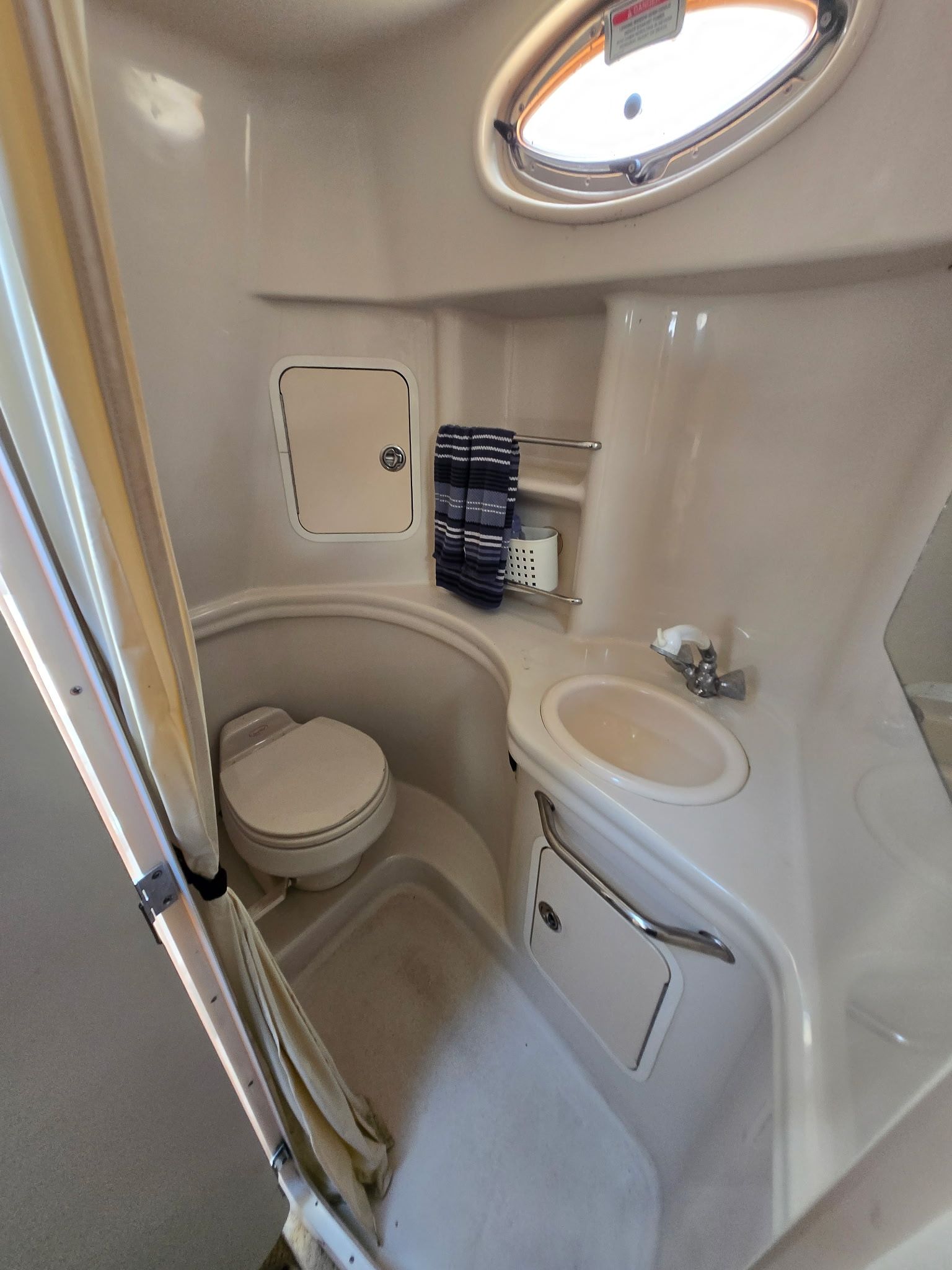 The image shows a compact boat bathroom with a toilet, sink, and porthole.