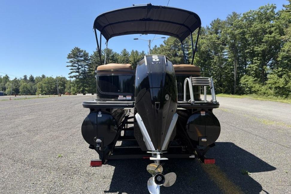2026 Regency 230 DL pontoon boat with canopy, parked on gravel, surrounded by trees.