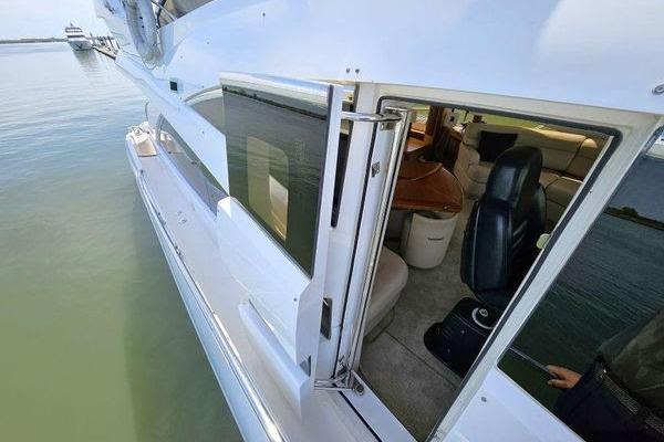 2005 Sunseeker Manhattan 66 yacht, side view with open cabin door, docked on calm water.