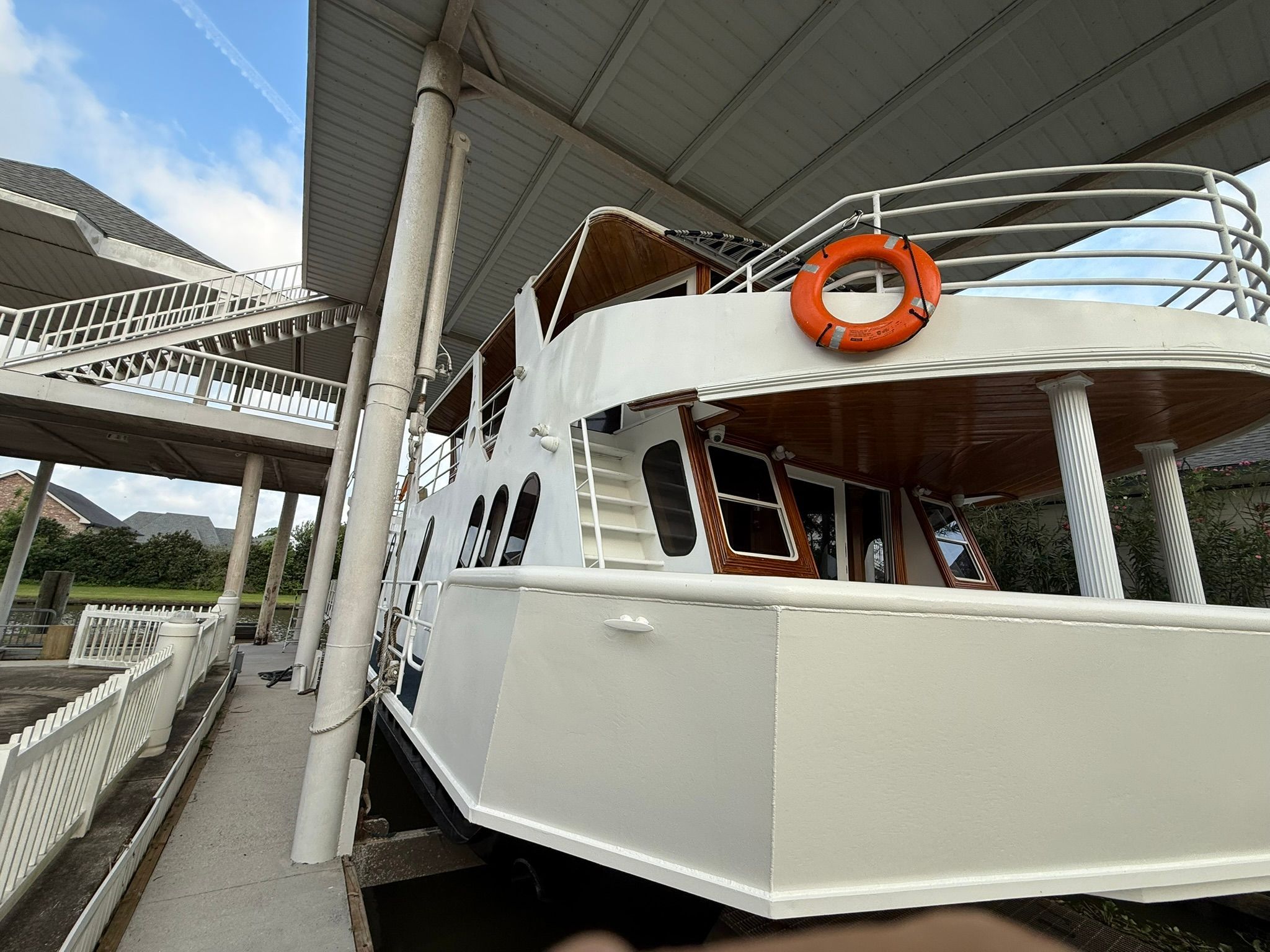 A white boat with an orange life ring is docked in a covered area.
