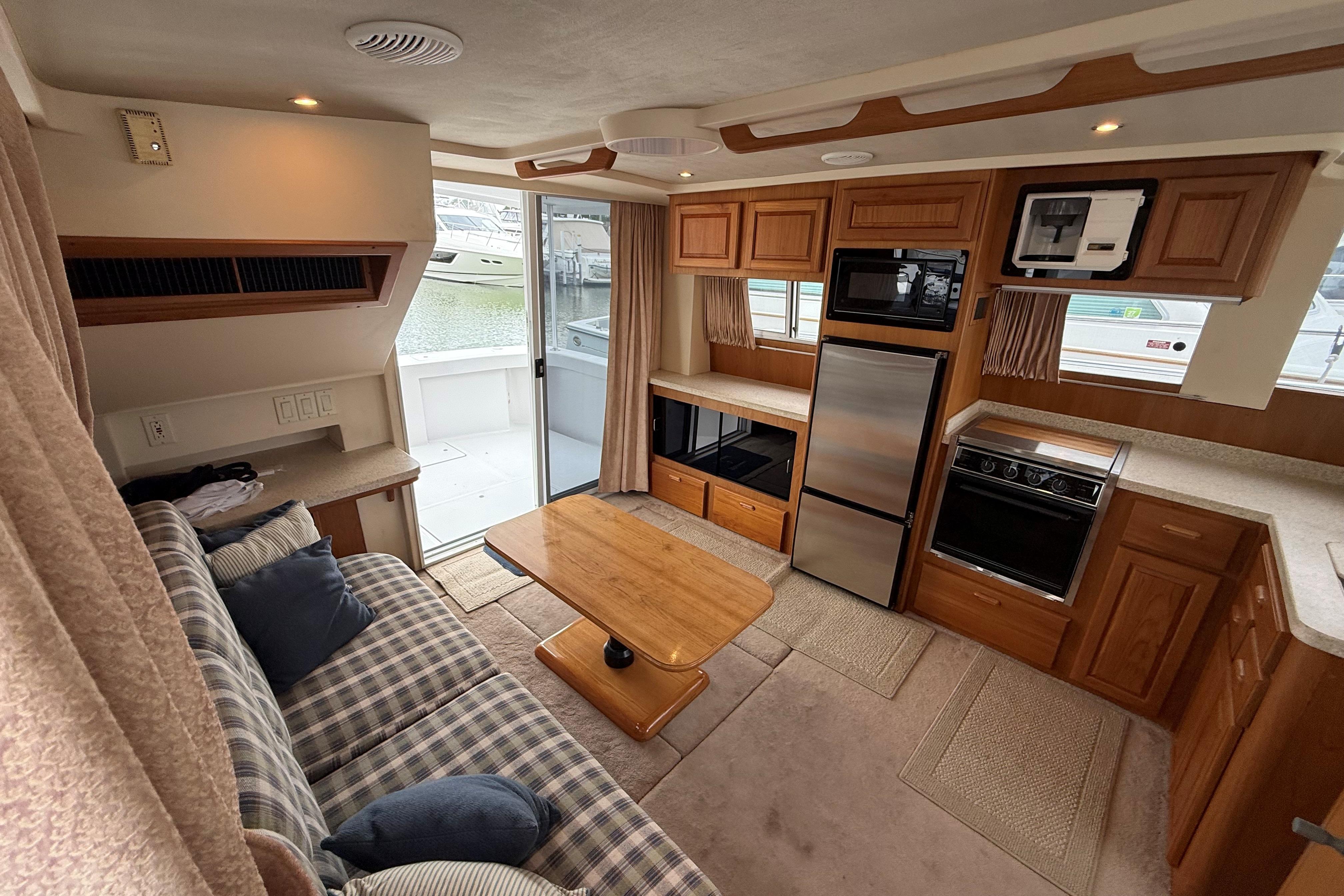 Interior of 1999 Mainship 350 Trawler with cozy seating, kitchen, and outdoor view.