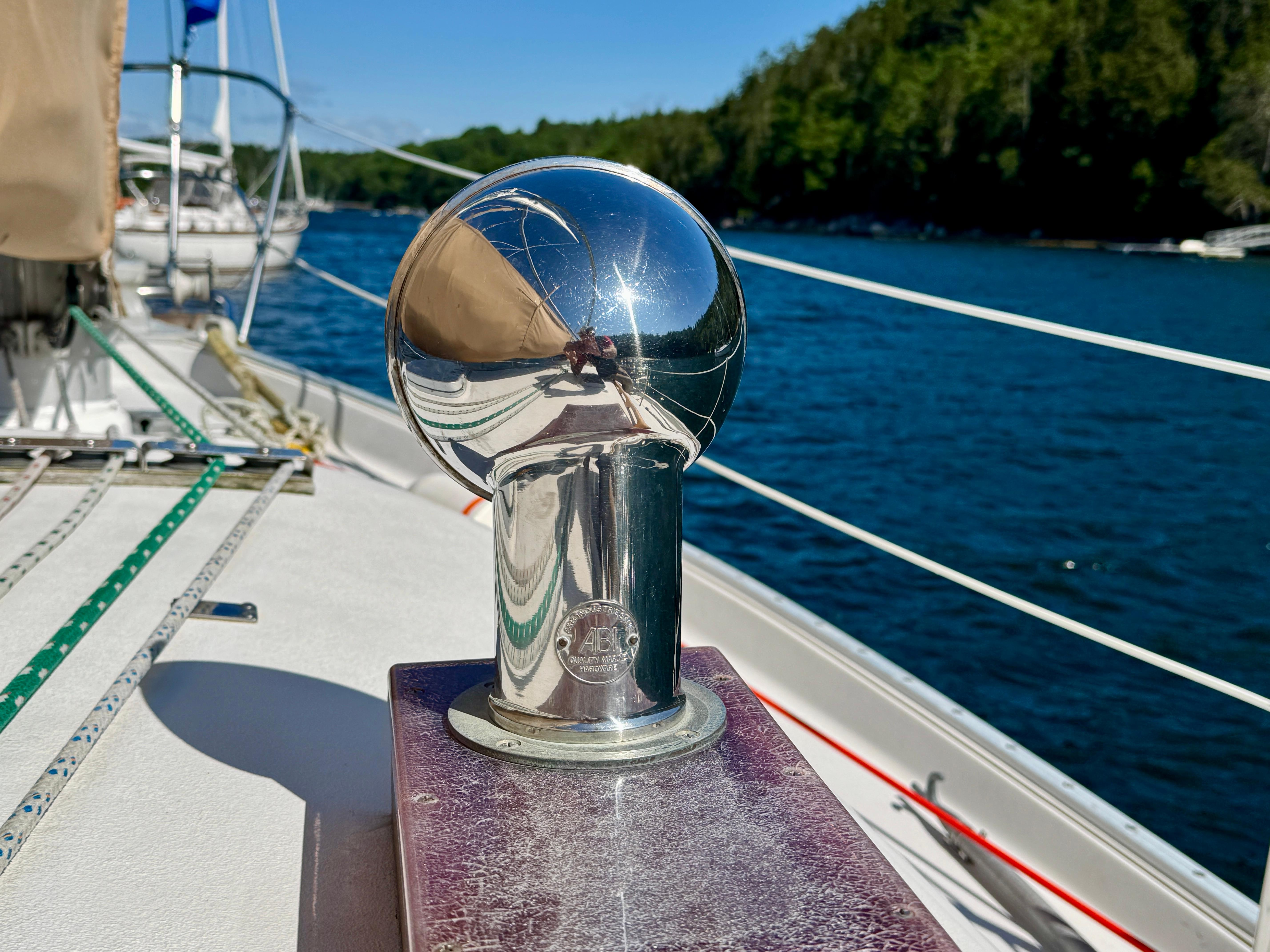Shiny metal fitting on 1989 Nonsuch 30 Ultra sailboat deck, with water and trees in background.