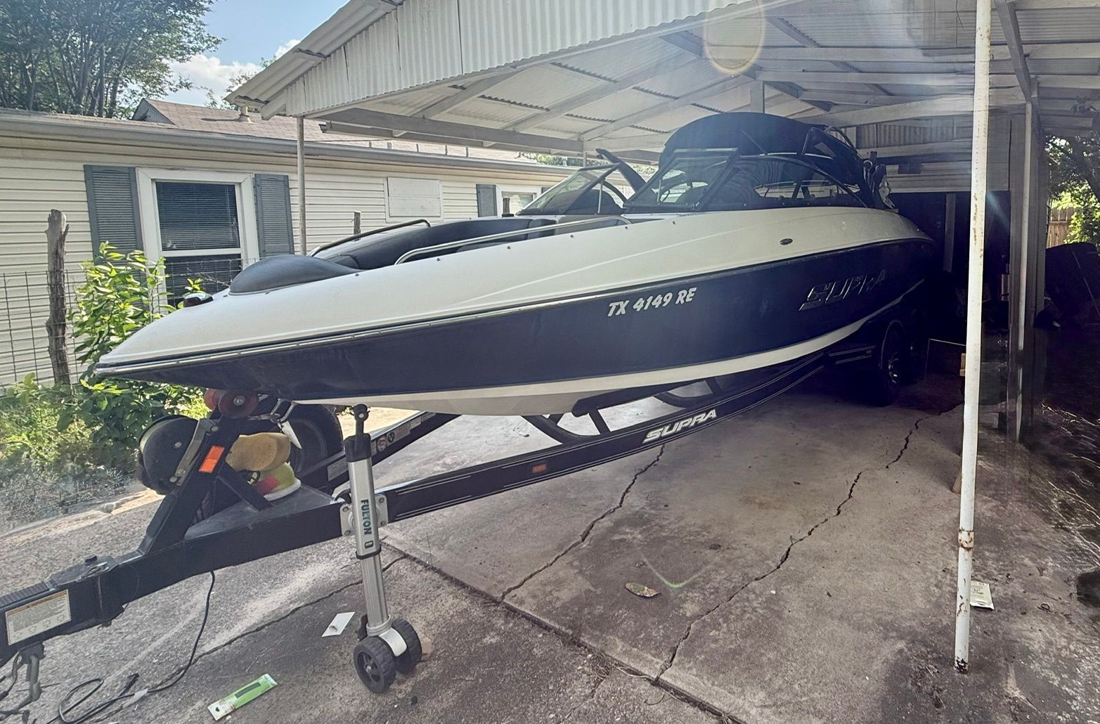 A 2012 Supra Launch 242 boat is on a trailer under a carport.