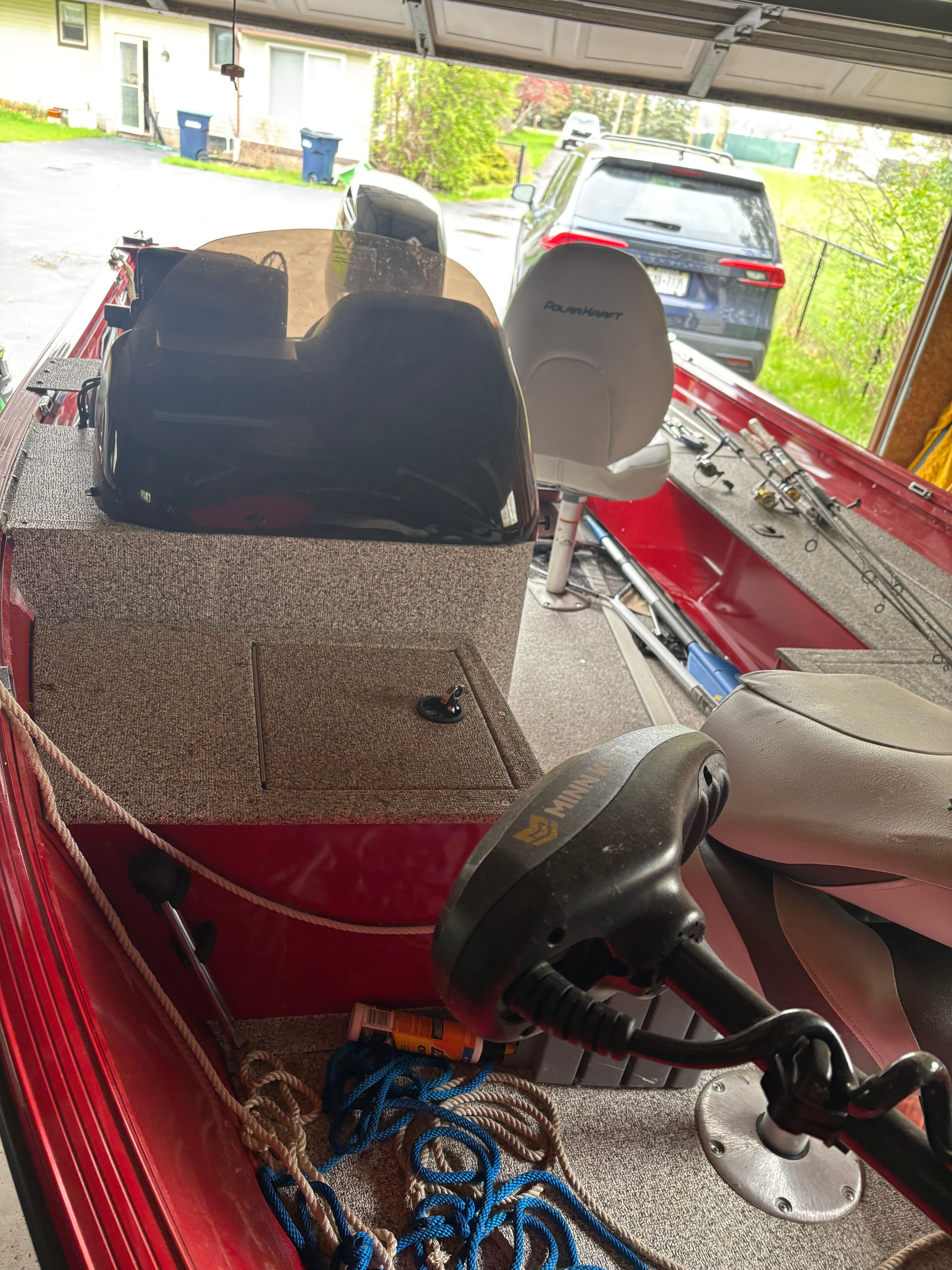 A red boat parked in a garage, featuring a helm station and a white seat.