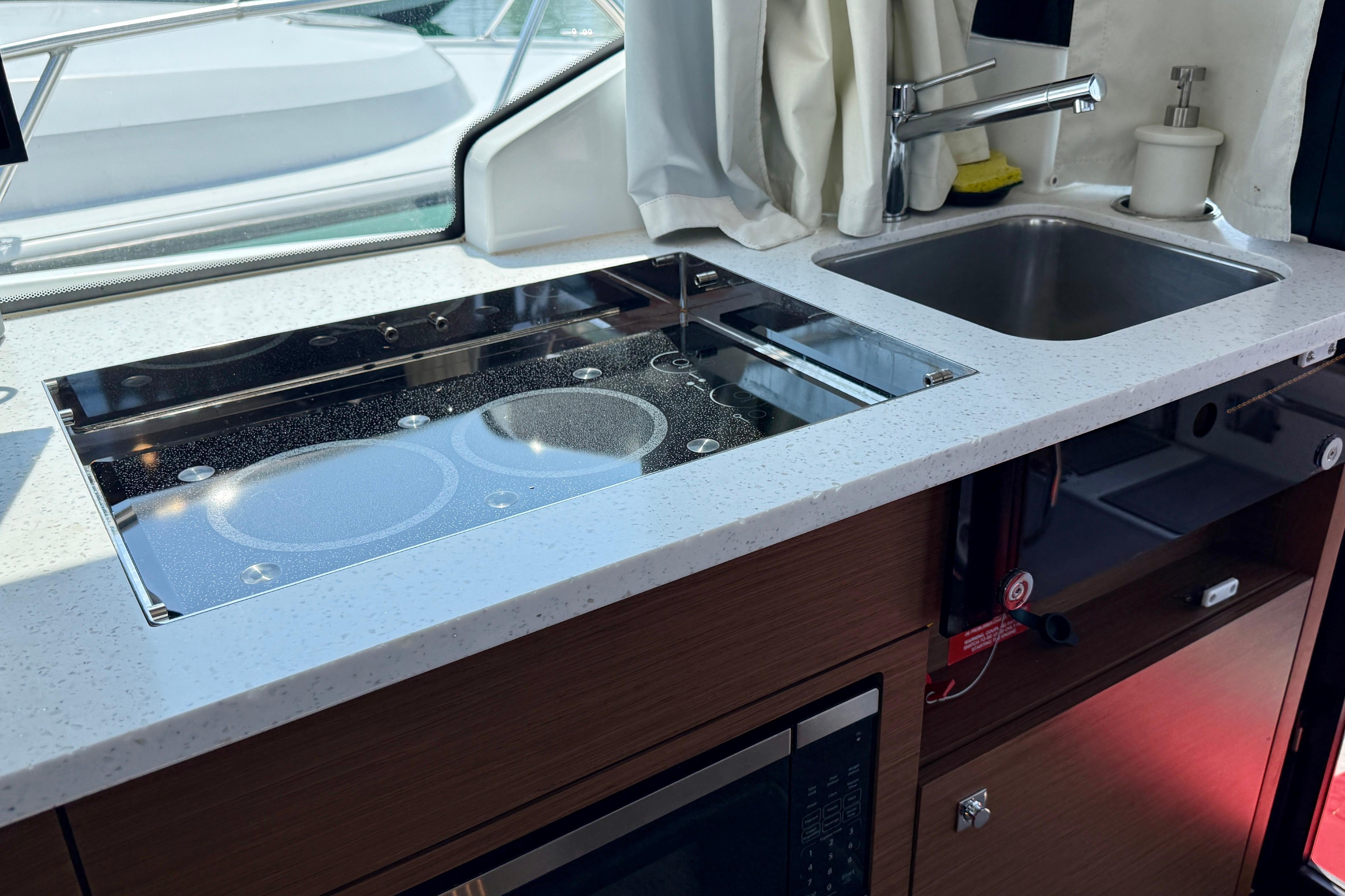 Modern kitchen area in 2022 Jeanneau NC 1095 Fly boat with stove and sink.