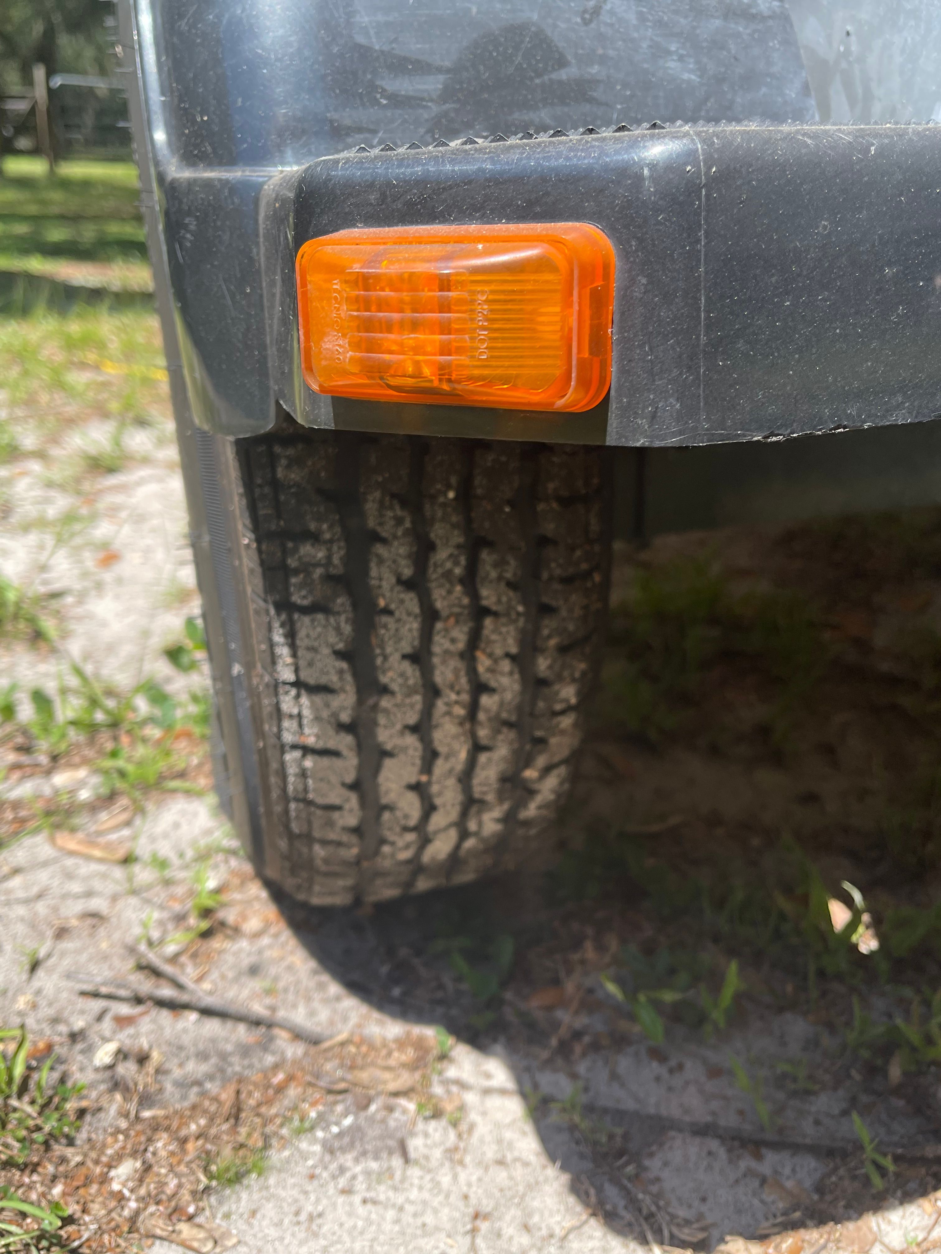 Close-up of a boat trailer with an orange reflector and a tire on sandy ground.