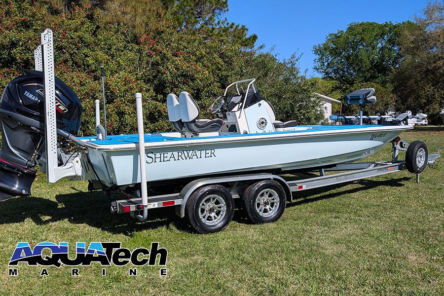 A 2023 ShearWater x22 boat on a trailer, surrounded by trees and grass.