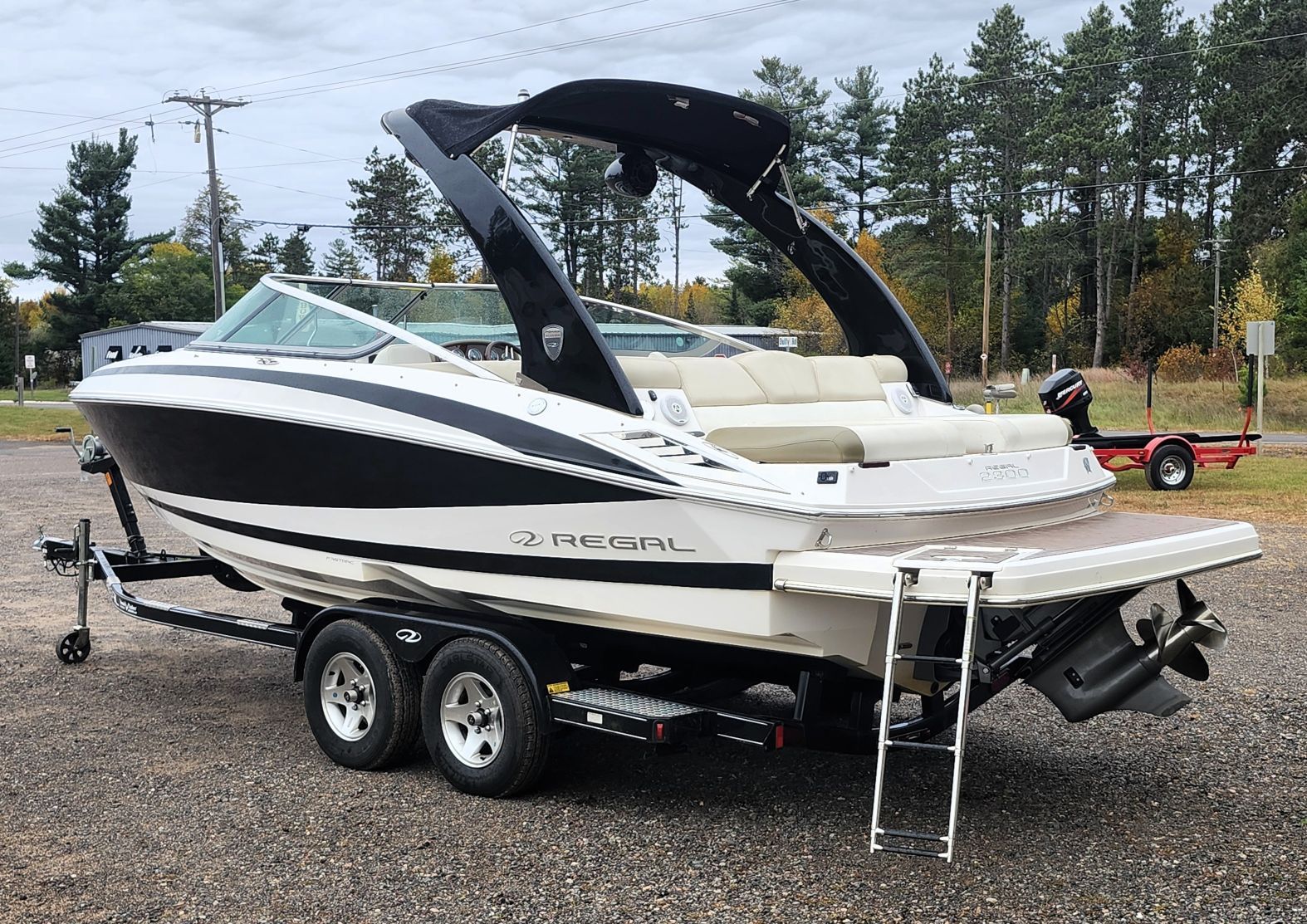 A white and black motorboat on a trailer, surrounded by trees and a cloudy sky.